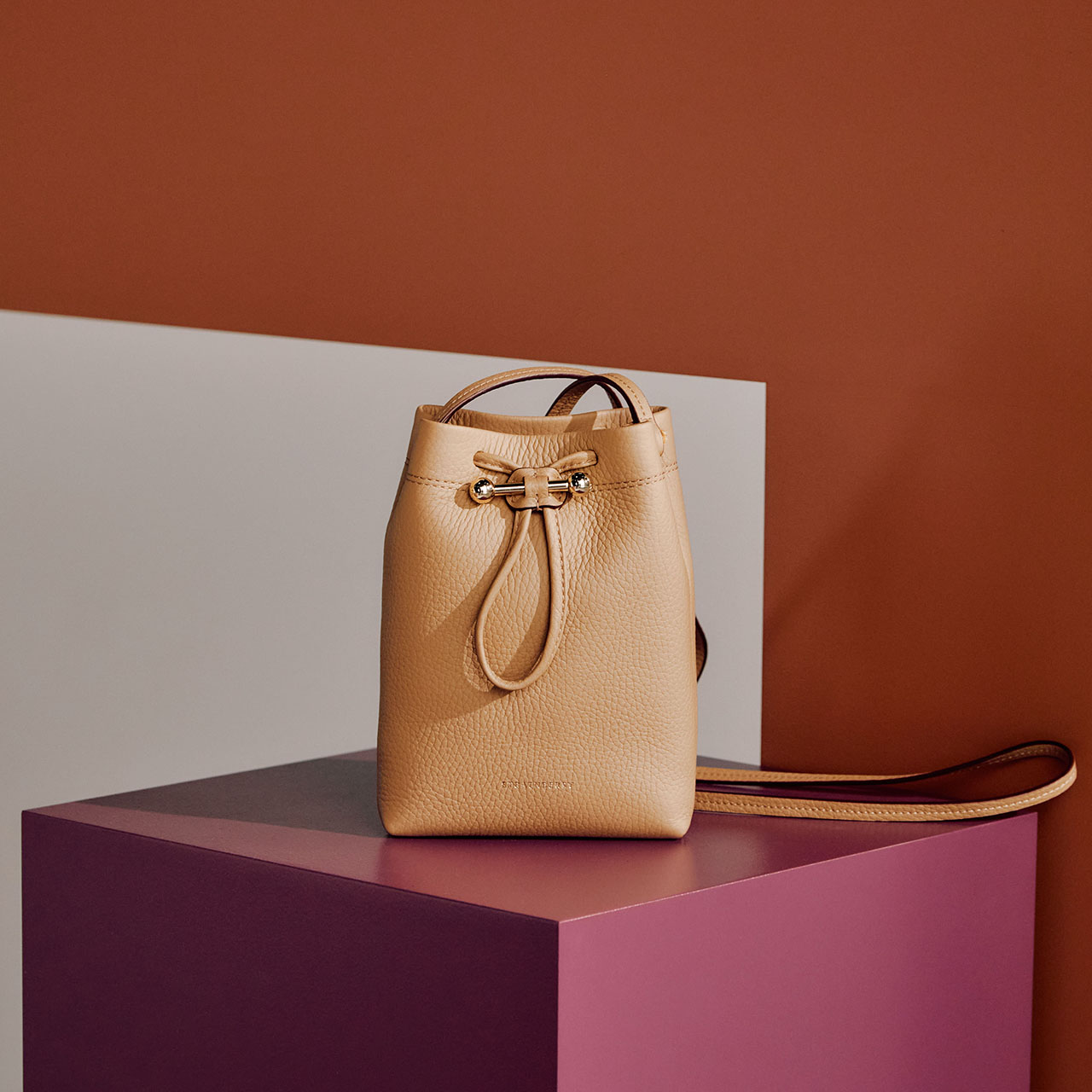 Beige leather bucket bag with gold hardware and brown shoulder strap on purple platform