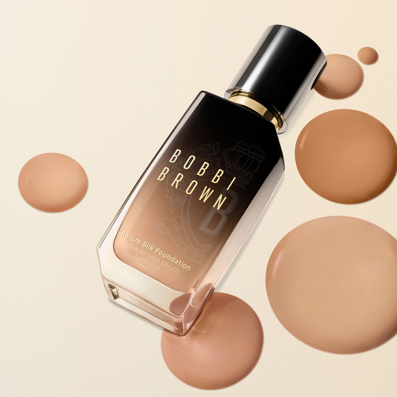 Bobbi Brown Serum Silk Foundation bottle with black cap and gold trim surrounded by beige foundation droplets on cream background.
