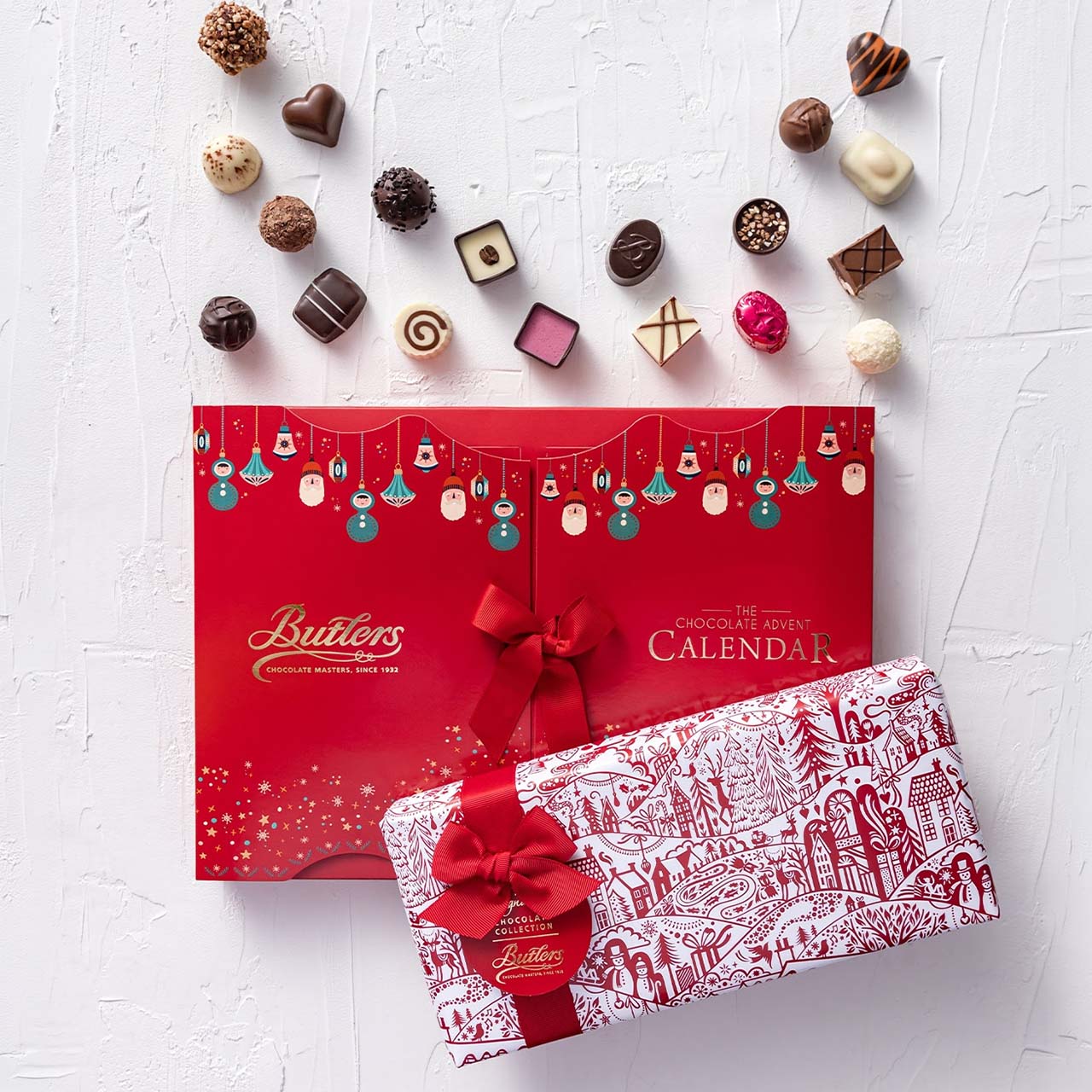 Assorted chocolates and gourmet treats displayed above red Butterscotch Chocolate Advent Calendars with festive hanging decorations and red ribbon bows