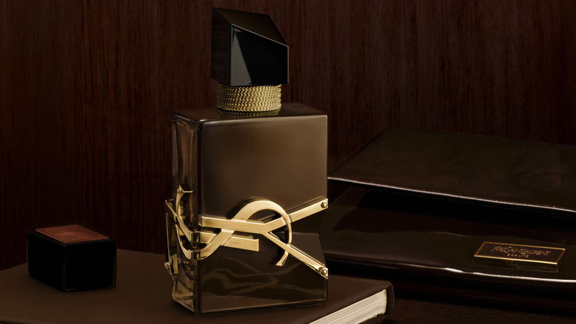 Yves Saint Laurent Libre Santal Couture fragrance bottle with black cap and gold bow detail displayed on dark table with wood backdrop.