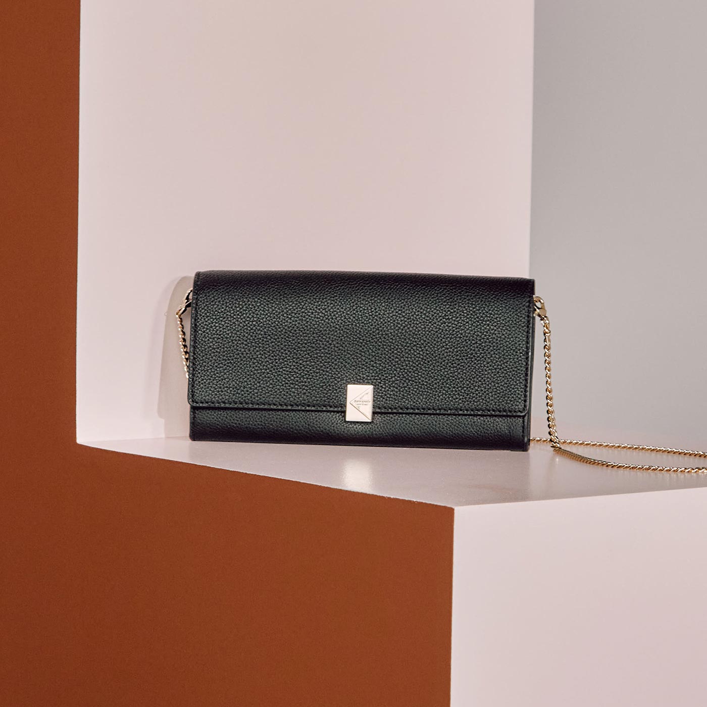 Black textured leather wallet with chain strap and metallic clasp on neutral background