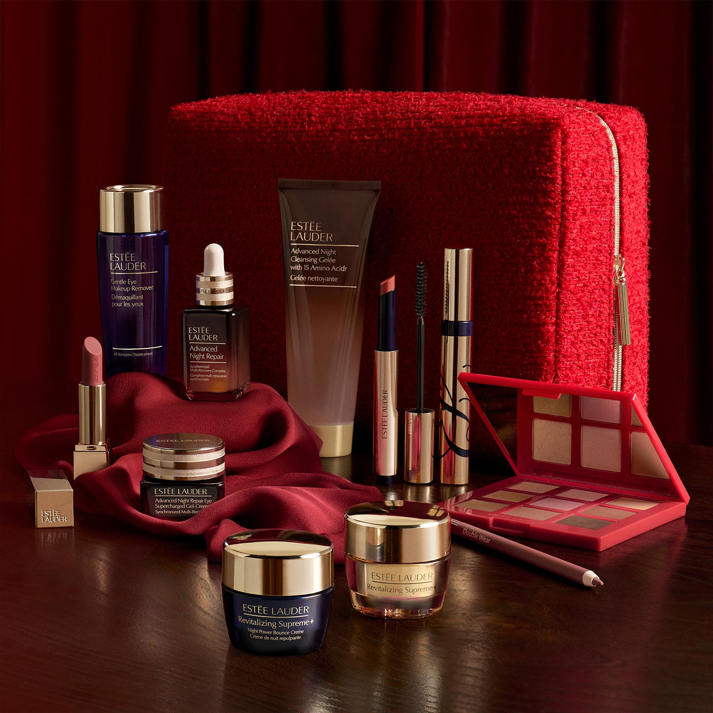 Est&eacute;e Lauder beauty collection including skincare, lipstick, mascara and eyeshadow palette on red background