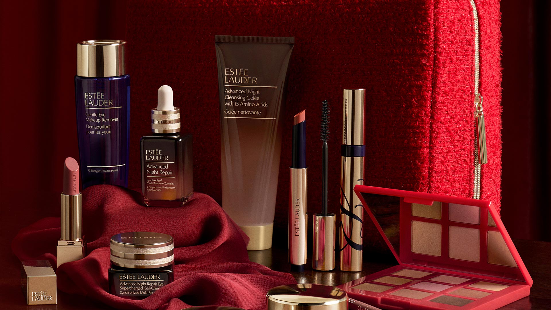 Estée Lauder beauty collection including skincare, lipstick, mascara and eyeshadow palette on red background