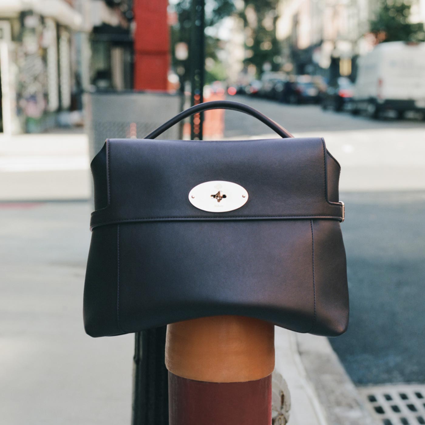 Navy leather handbag with white oval clasp detail on urban street background
