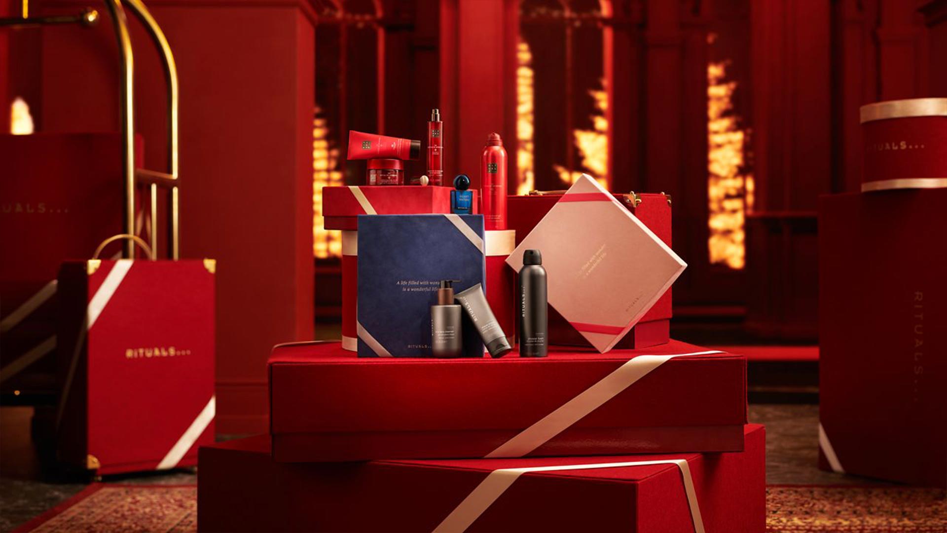 Luxury beauty gift sets displayed on red tiered platforms with gold accents and warm lighting, including red and nude cosmetic products