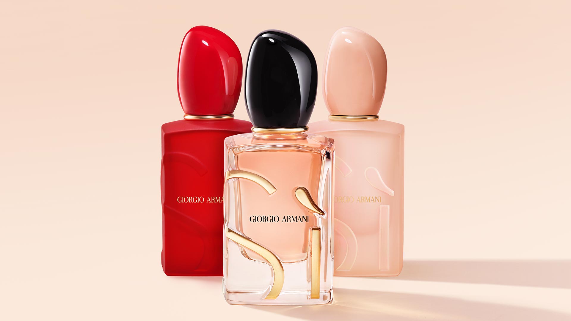 Three Giorgio Armani fragrance bottles in red, black, and pink with rounded caps on beige background