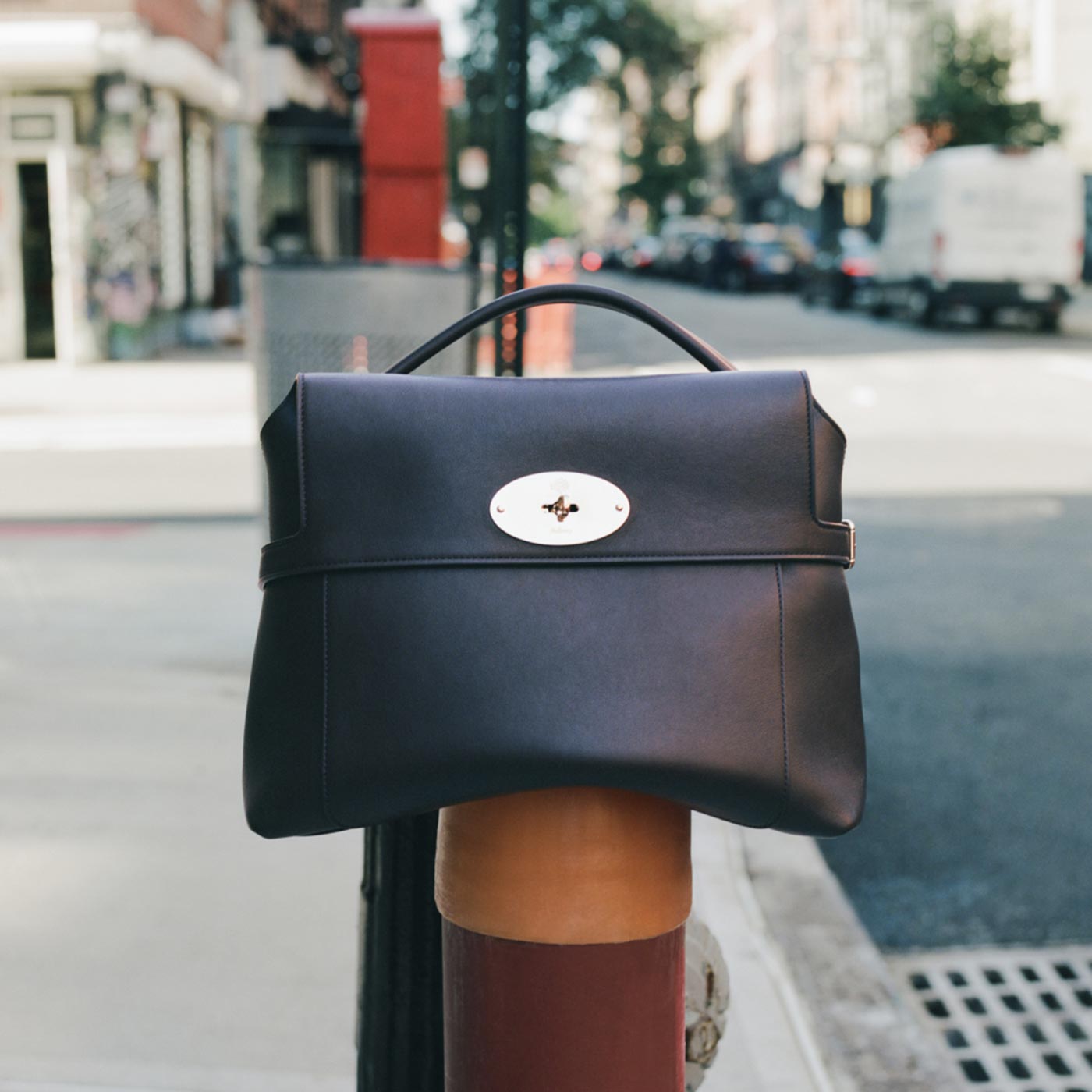 Black leather structured handbag with metal turnlock clasp displayed on urban street
