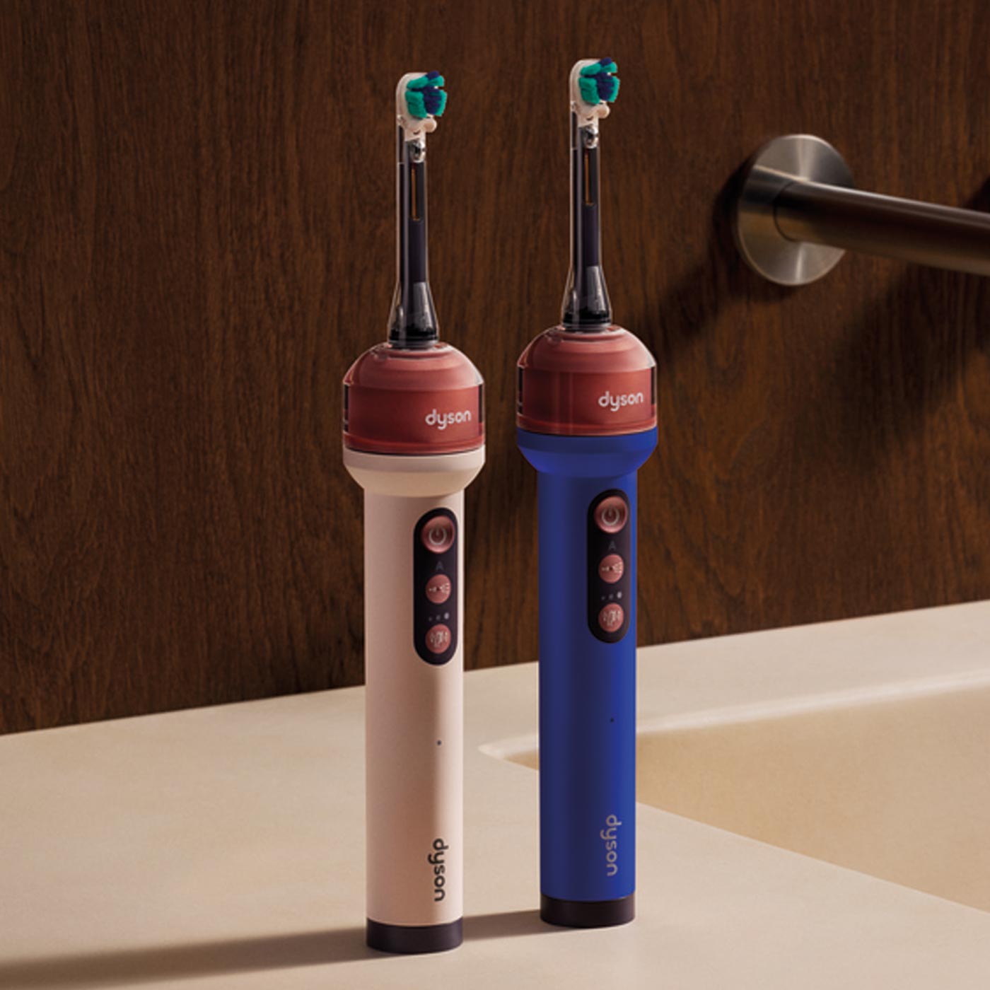 Two Dyson electric toothbrushes in cream and blue with teal brush heads positioned on bathroom sink