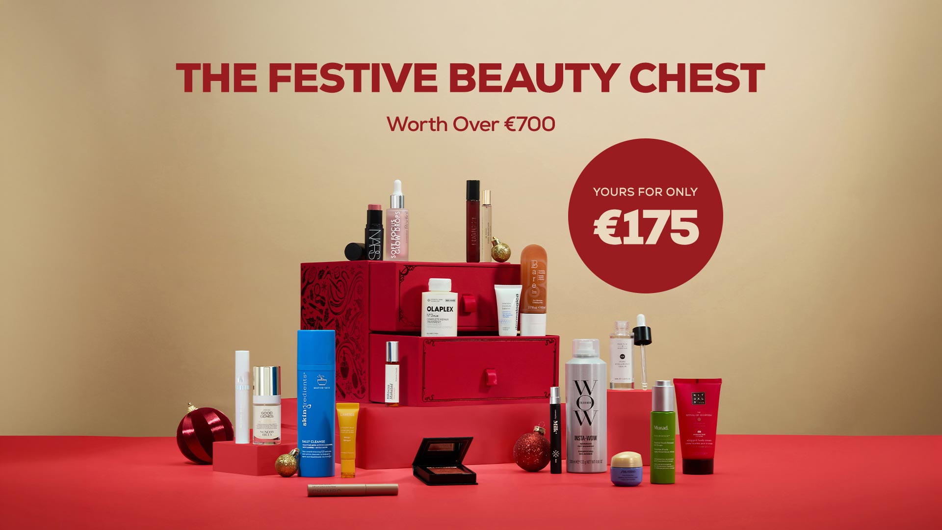 Red tiered gift chest filled with assorted beauty and skincare products, surrounded by festive baubles and cosmetics, worth over €700