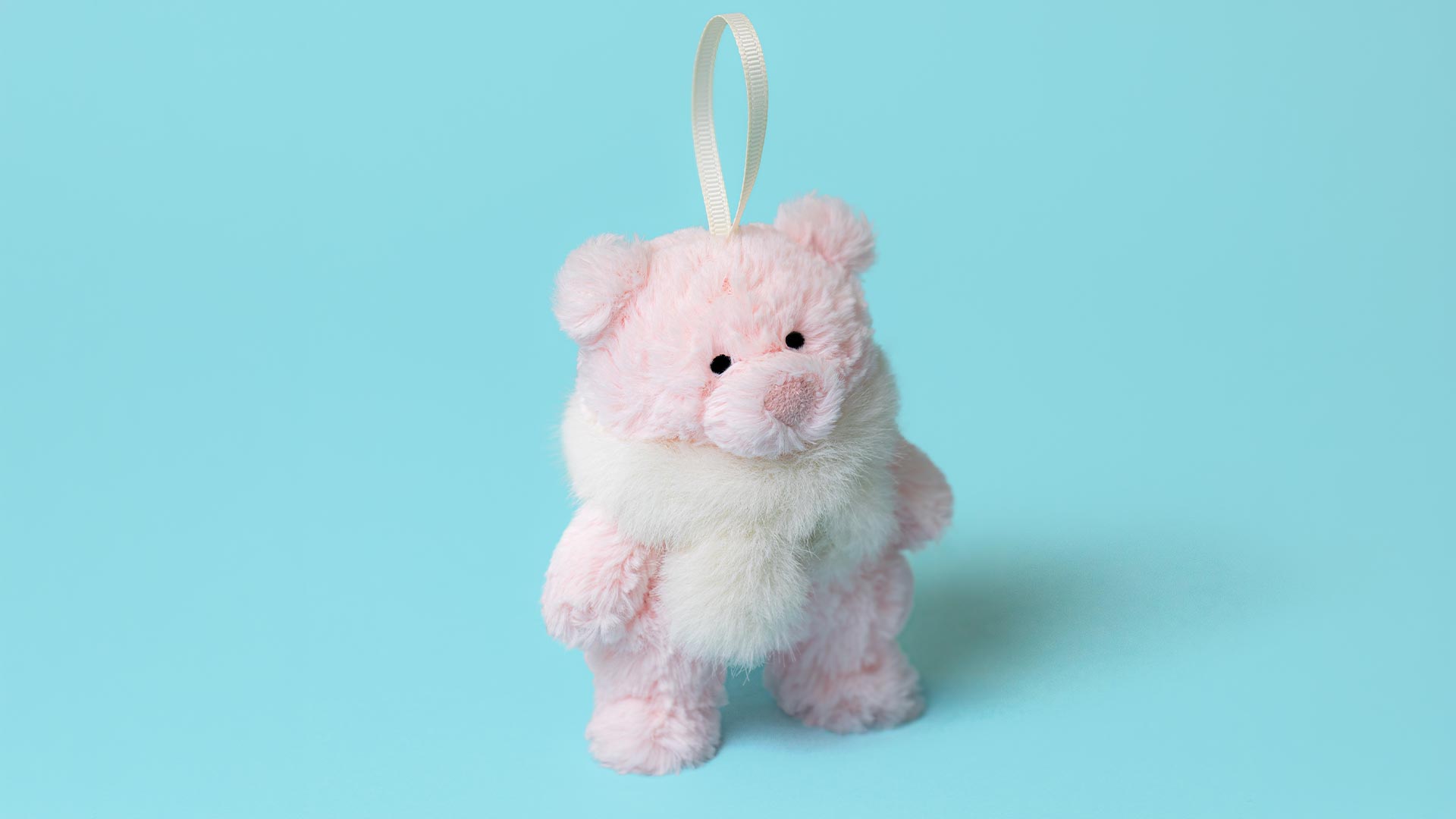 Pink and white fluffy teddy bear plush toy with ribbon loop hanging attachment against turquoise background
