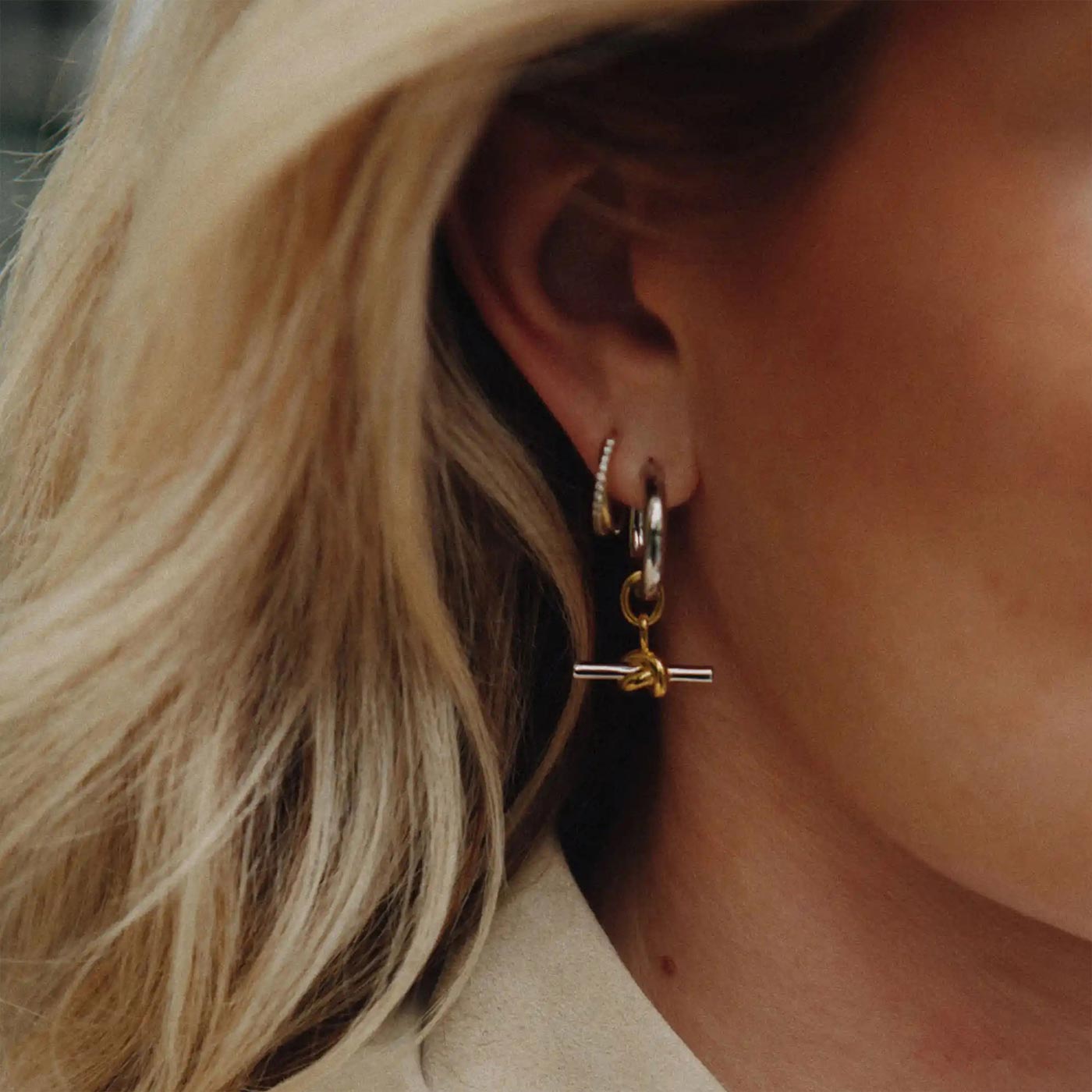 Close-up of woman wearing mixed metal hoop earrings with gold cross charm detail