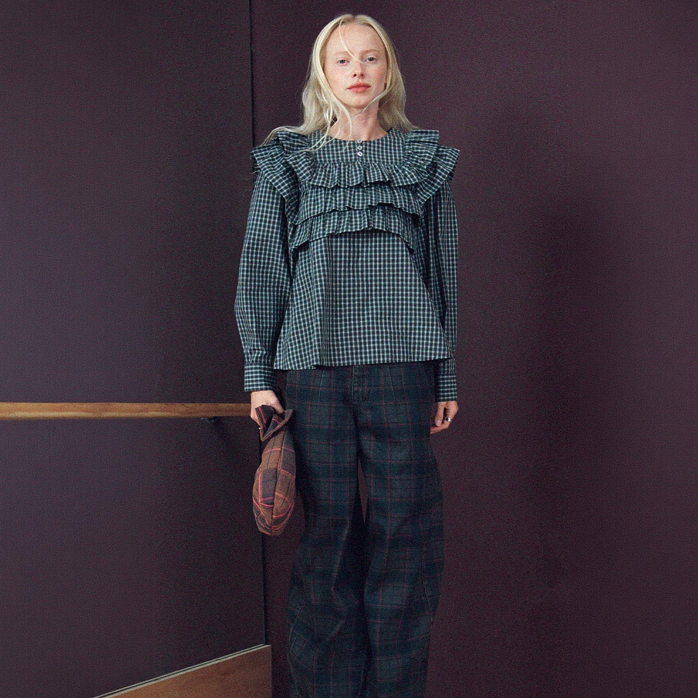 Woman wearing teal gingham checked blouse with ruffled collar, dark tartan trousers, and pink platform sandals