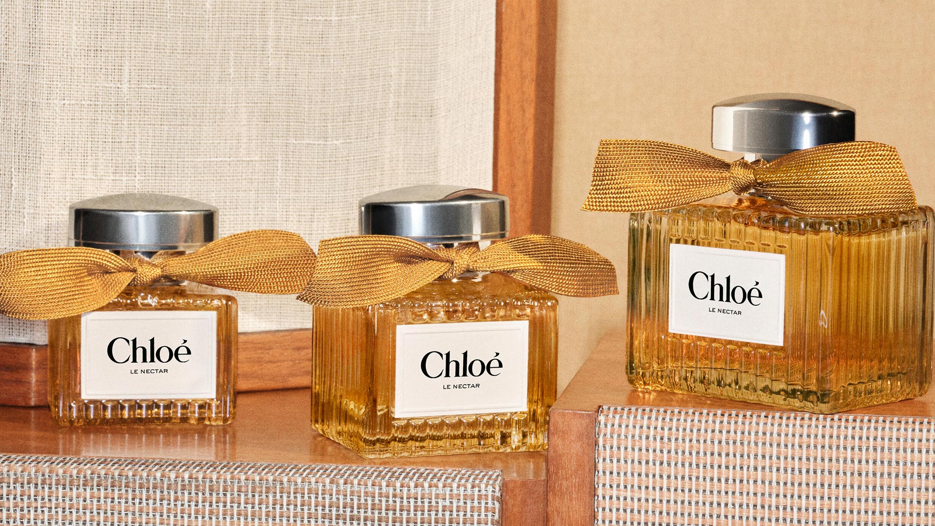 Three Chloé Le Nectar fragrance bottles with gold ribbon bows displayed on wooden surface