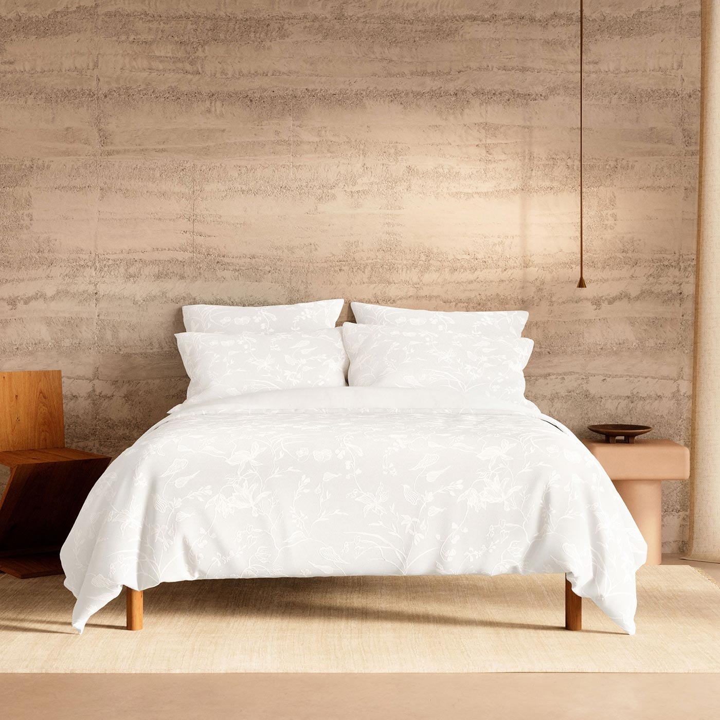 Bed with white embroidered duvet and pillows in minimalist bedroom with textured beige wall