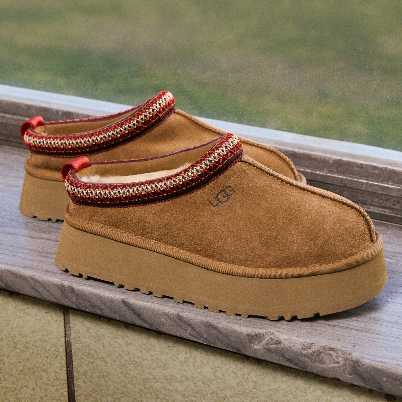 Pair of tan suede platform clogs with red and cream knitted ankle straps on wooden surface