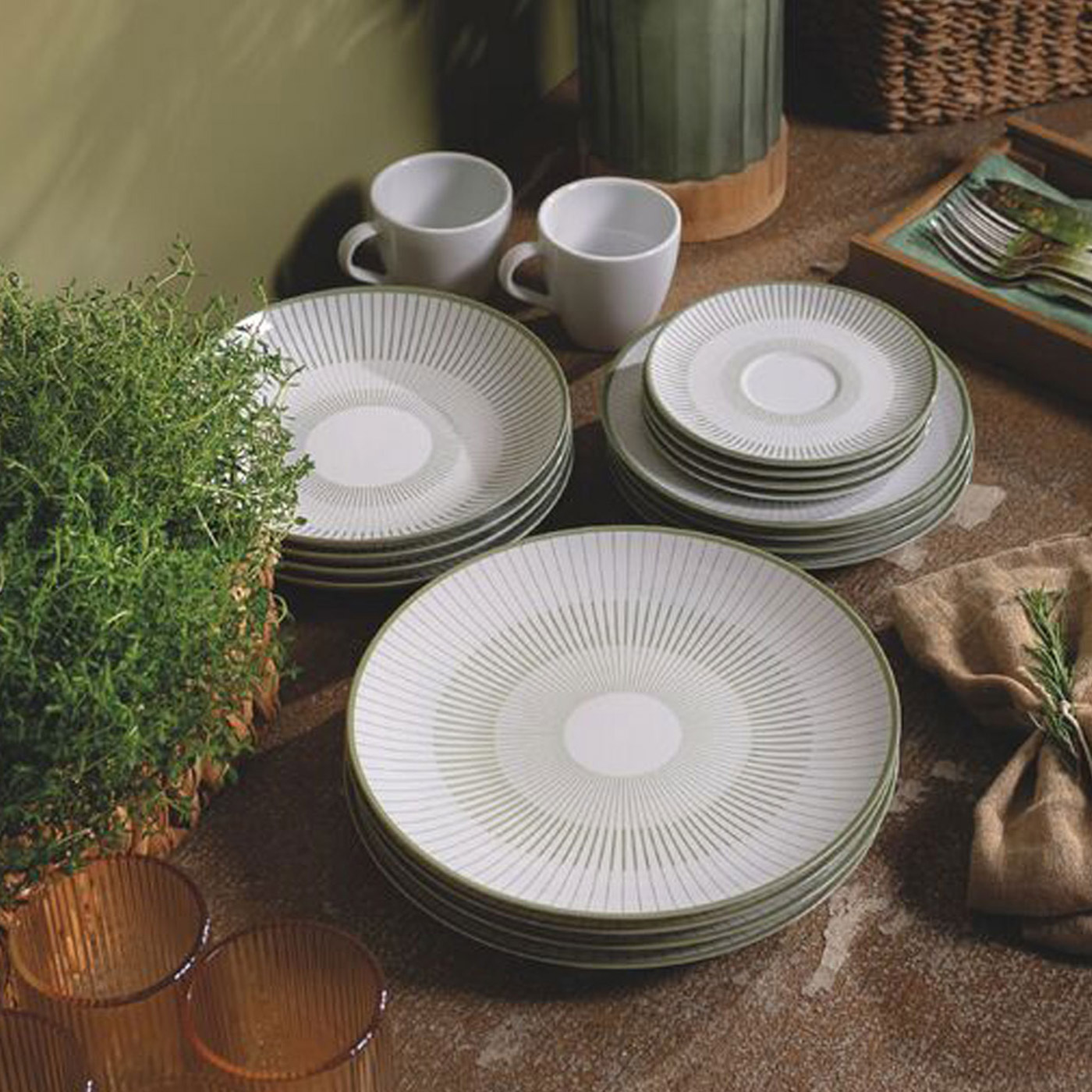 Stacked white striped dinner plates and side plates with white mugs, fresh herbs, and woven baskets on natural wood table