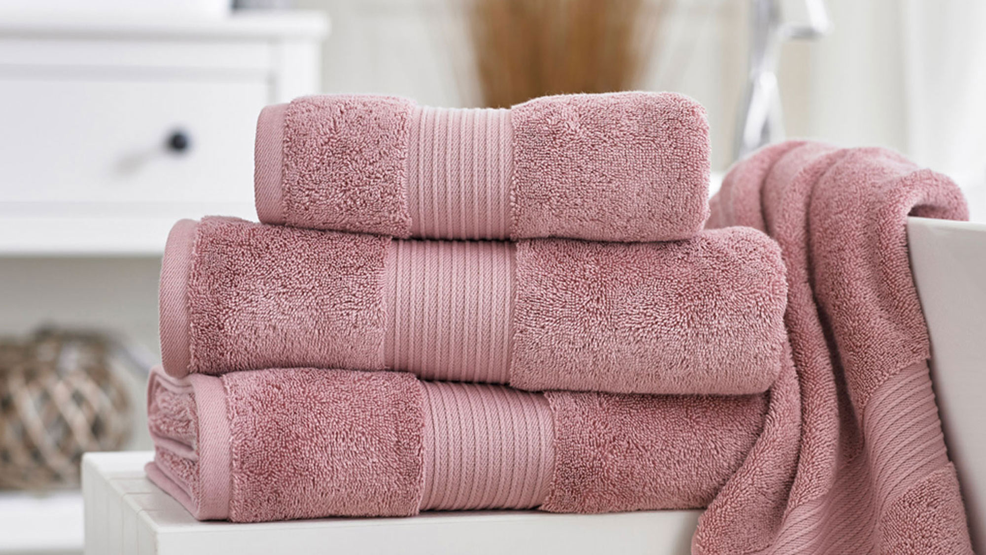 A stack of pink towels on a white bathroom bench with a towel hanging beside them.
