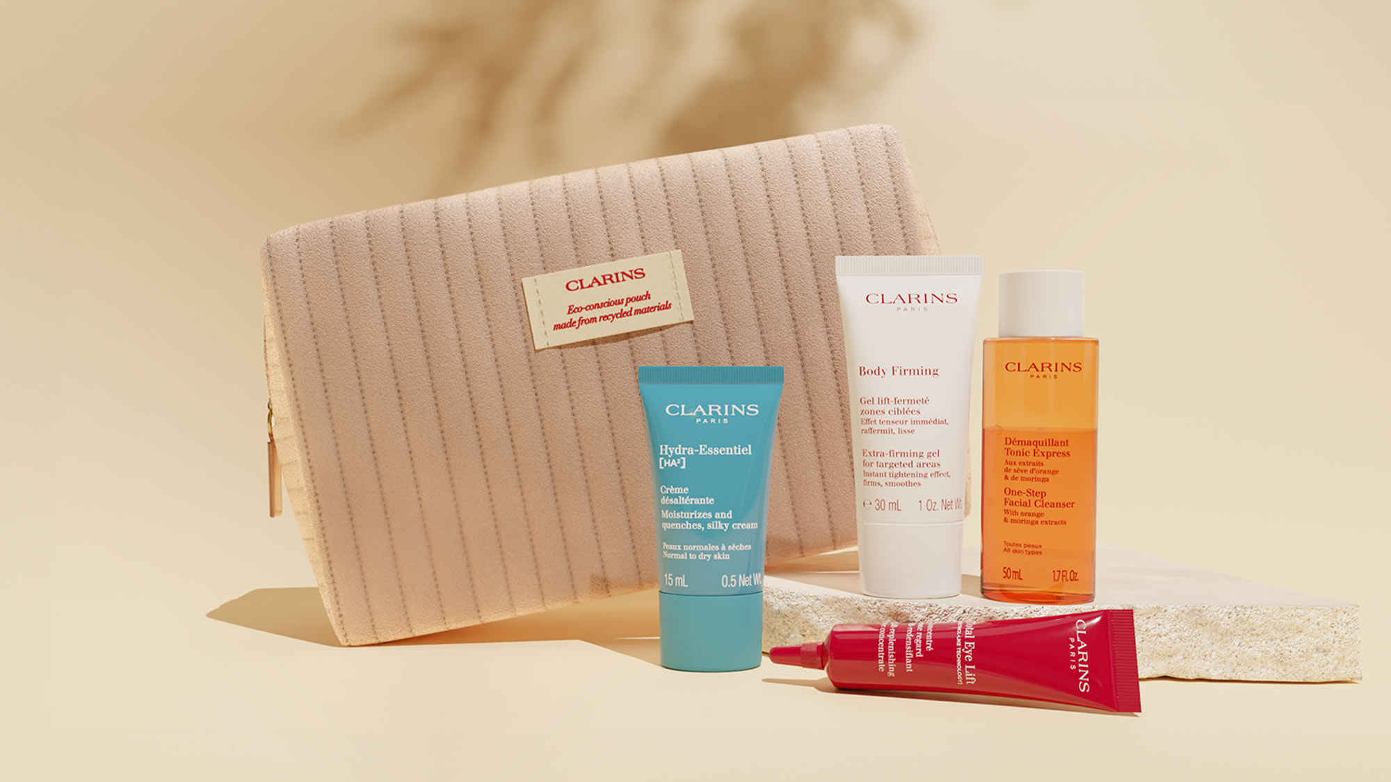 A collection of Clarins skincare products displayed alongside a textured beige pouch on a neutral background.