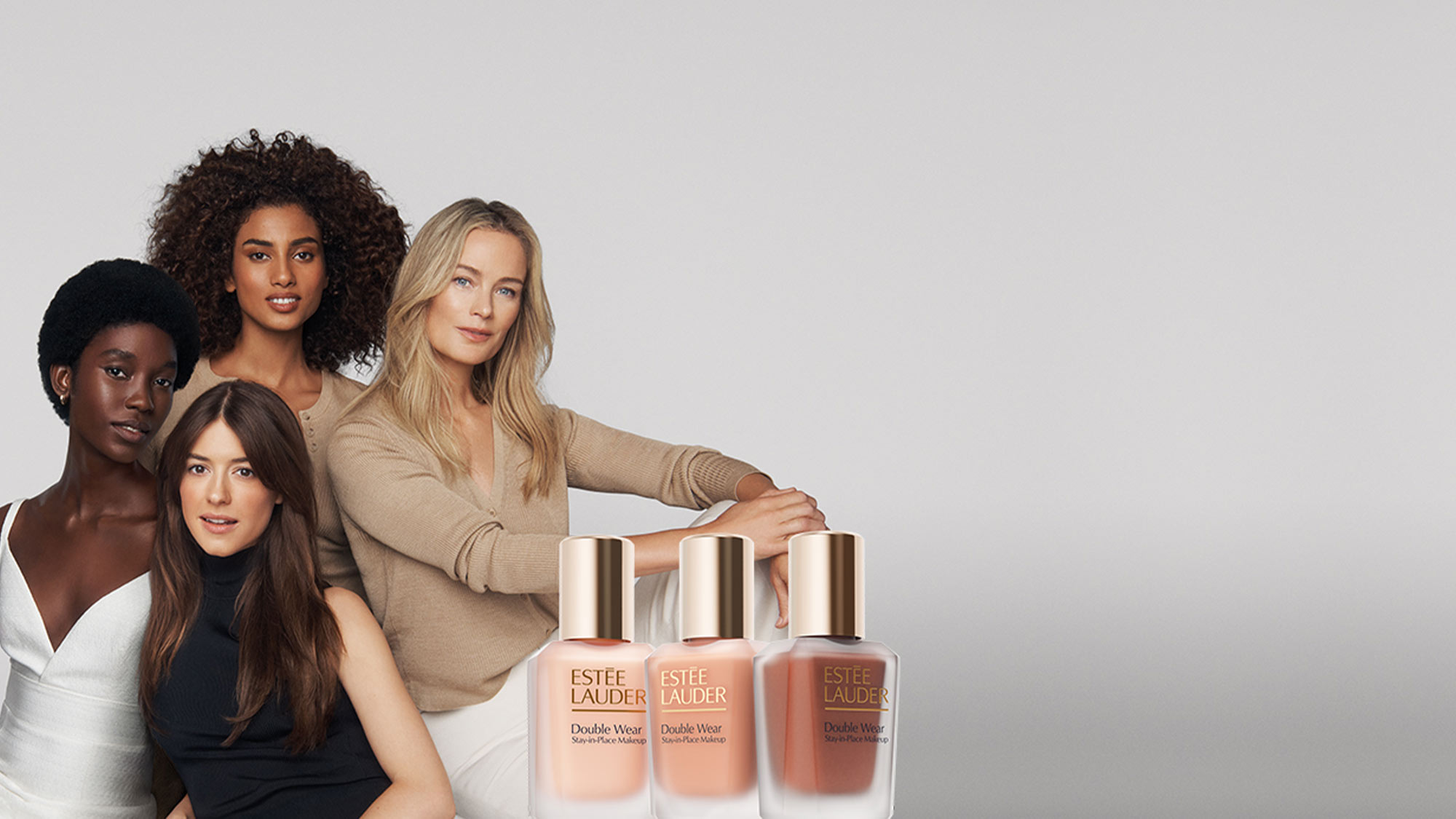 Four women posed together with three Estée Lauder Double Wear foundation bottles in the foreground.