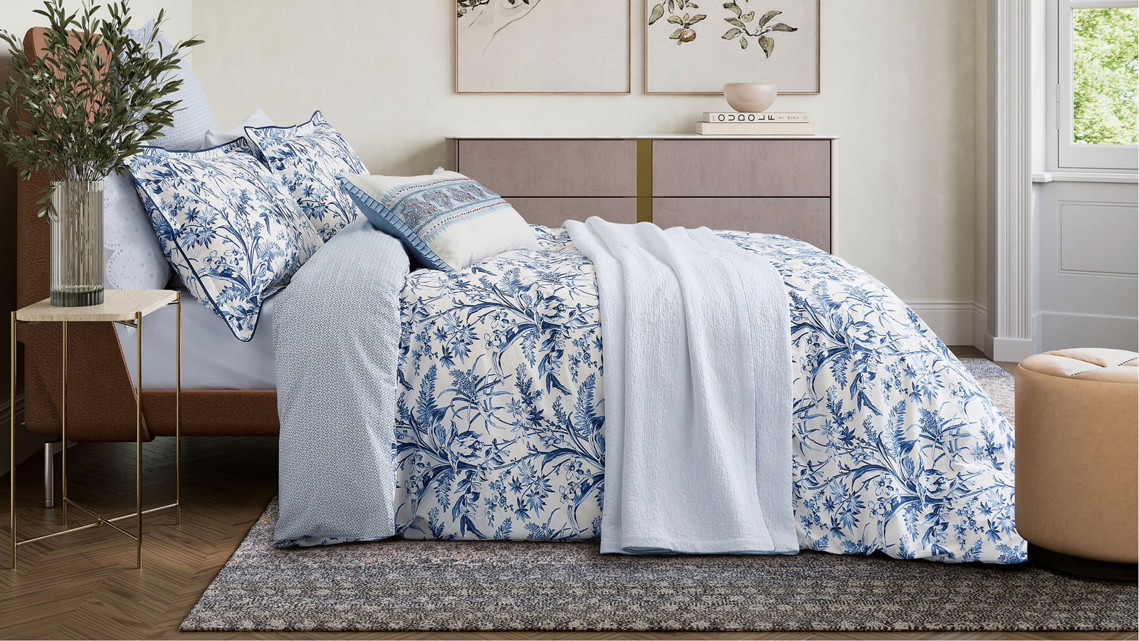 A cozy bedroom with a bed featuring light, floral-patterned bedding, a wooden headboard, and a large window.