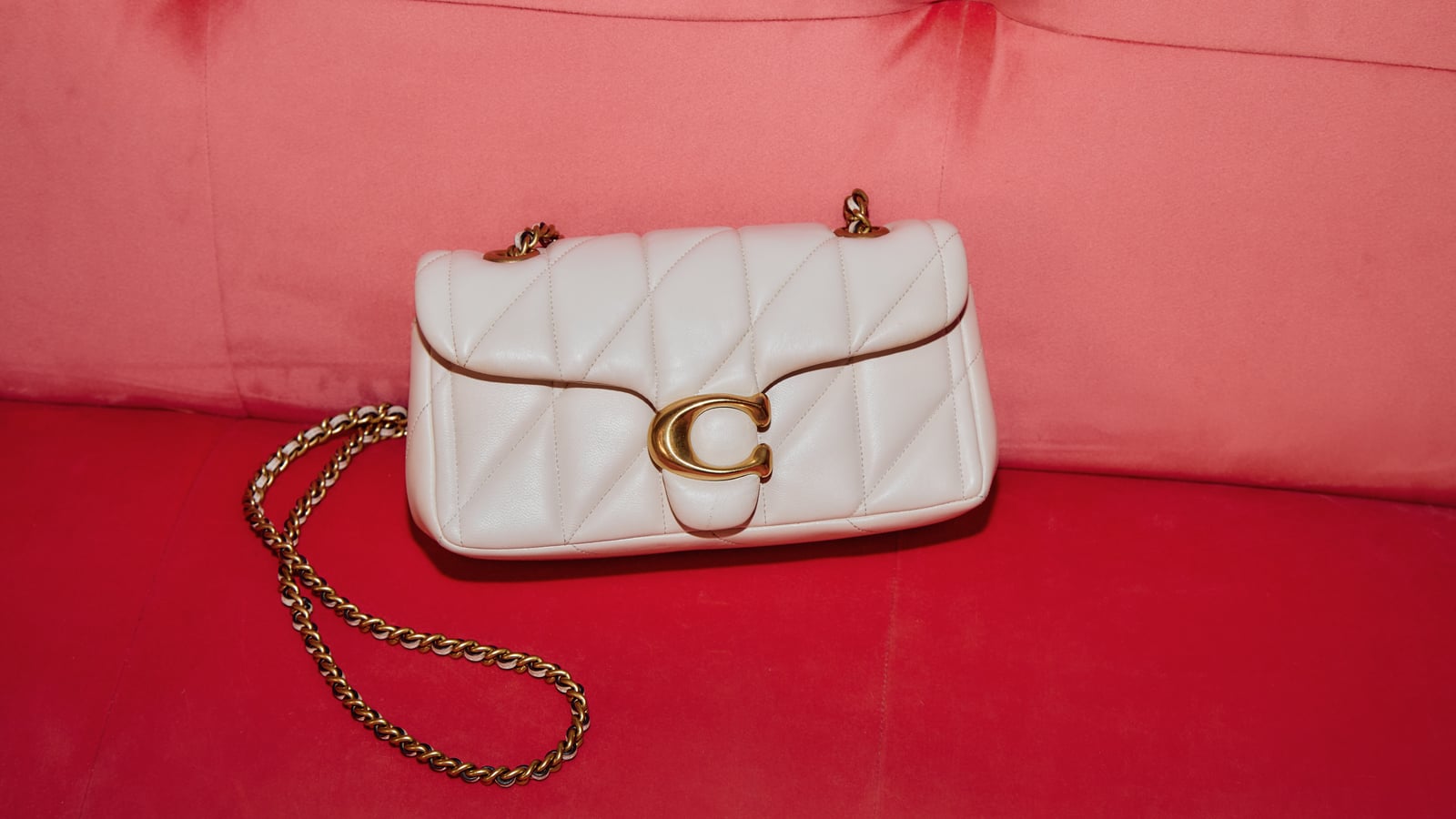 A white quilted handbag with a gold chain and clasp on a red and pink sofa.
