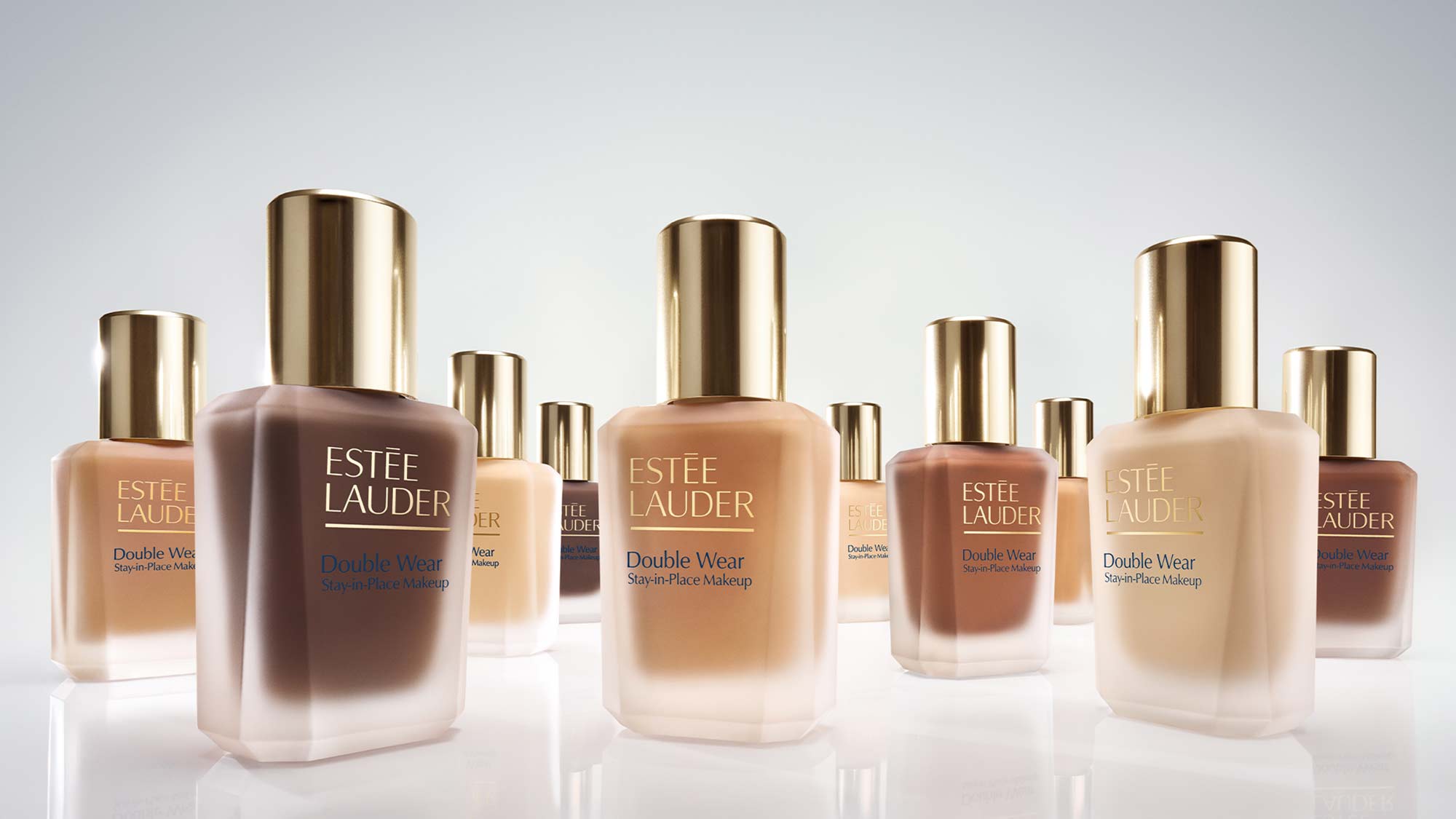 A bottle of Estée Lauder Double Wear foundation next to a light blue makeup sponge on a reflective surface.