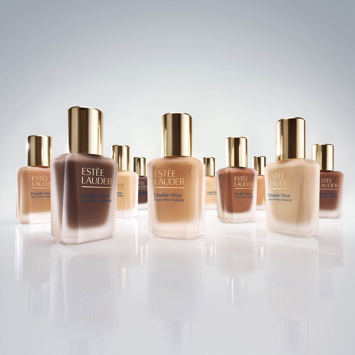 A bottle of Estée Lauder Double Wear foundation next to a light blue makeup sponge on a reflective surface.