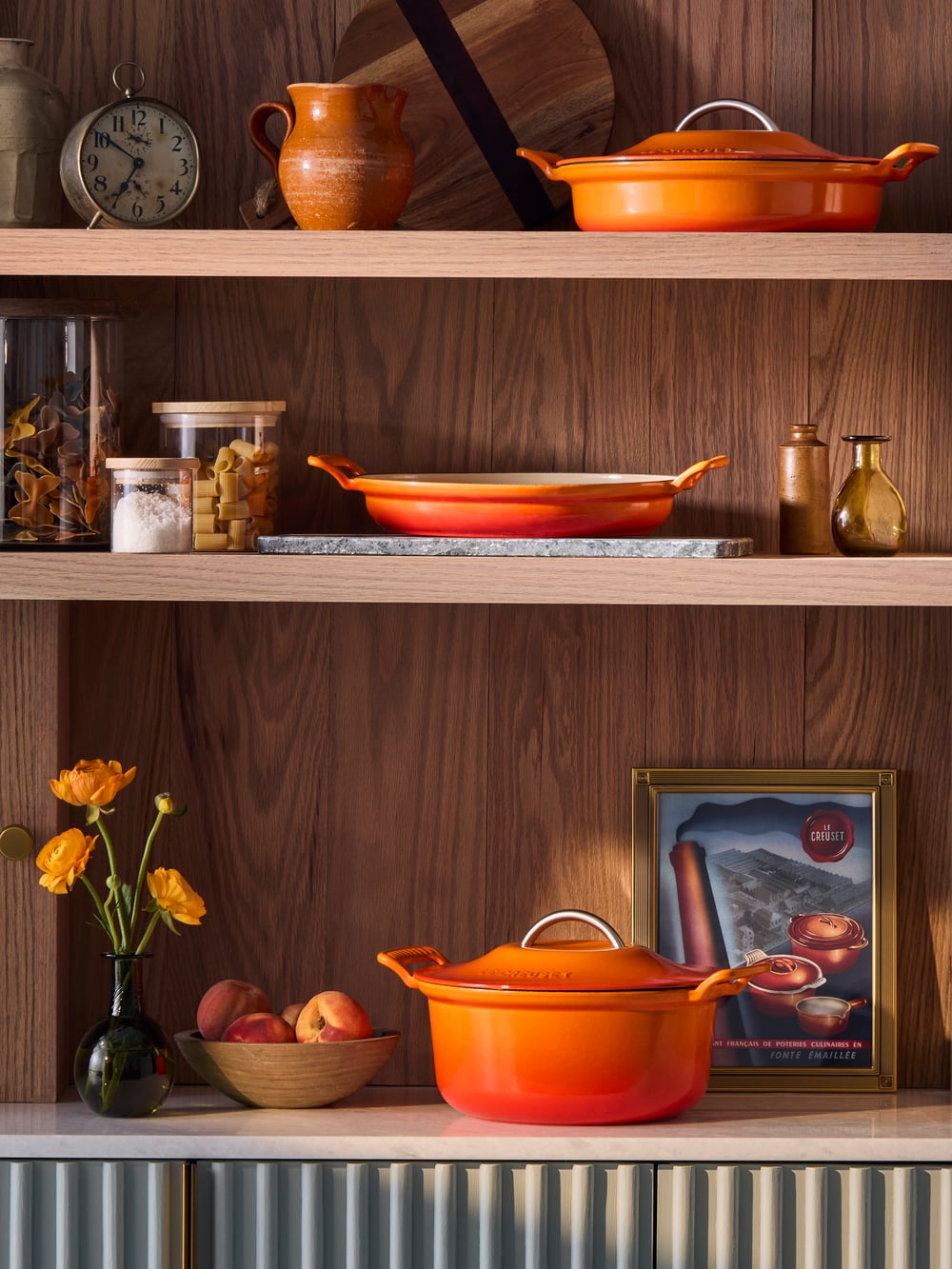 Wooden shelf with a red dish, spice jars, flowers, and a framed picture.