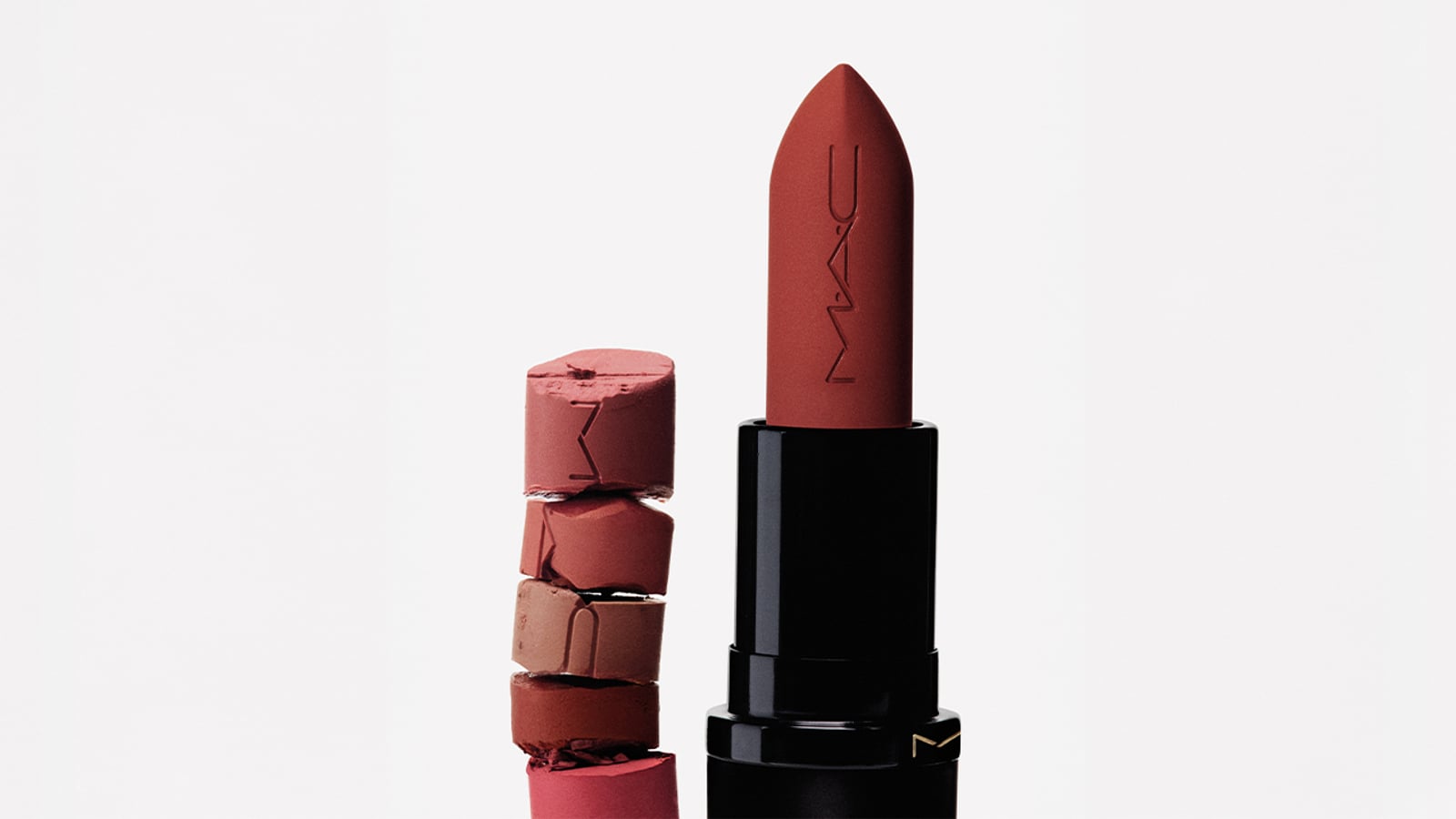 A red lipstick with 'MAC' embossed, next to broken lipstick pieces stacked vertically.