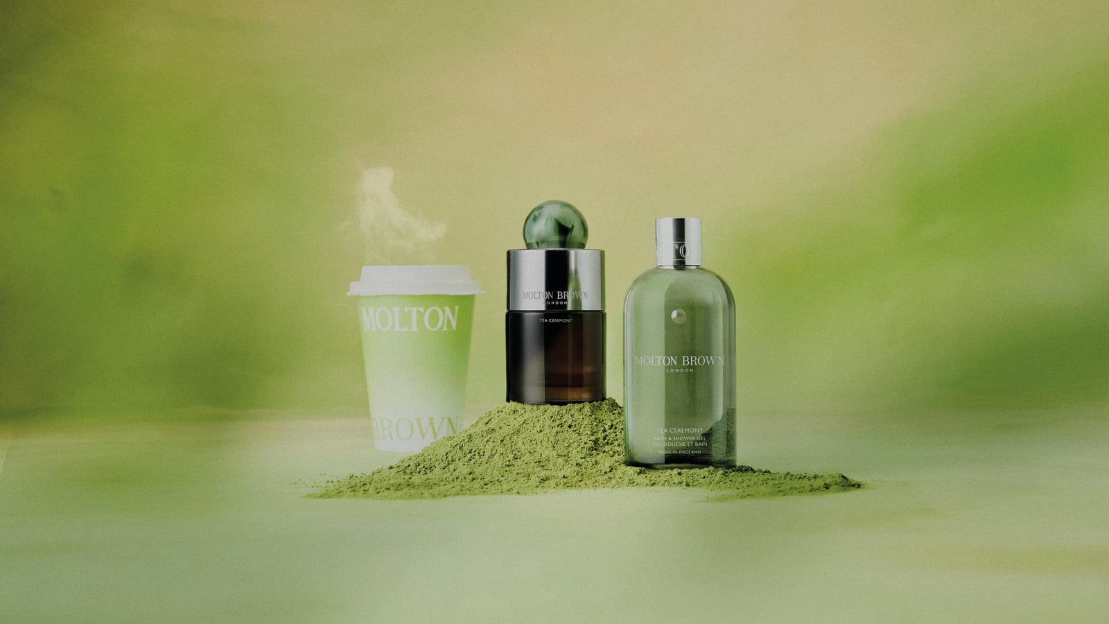A coffee cup and two Molton Brown products on a mound of green powder against a green background.