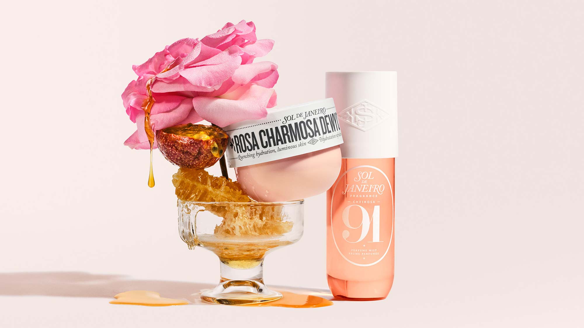 A floral-themed Sol de Janeiro cosmetic display with a rose, honeycomb, and bottle on a glass pedestal.