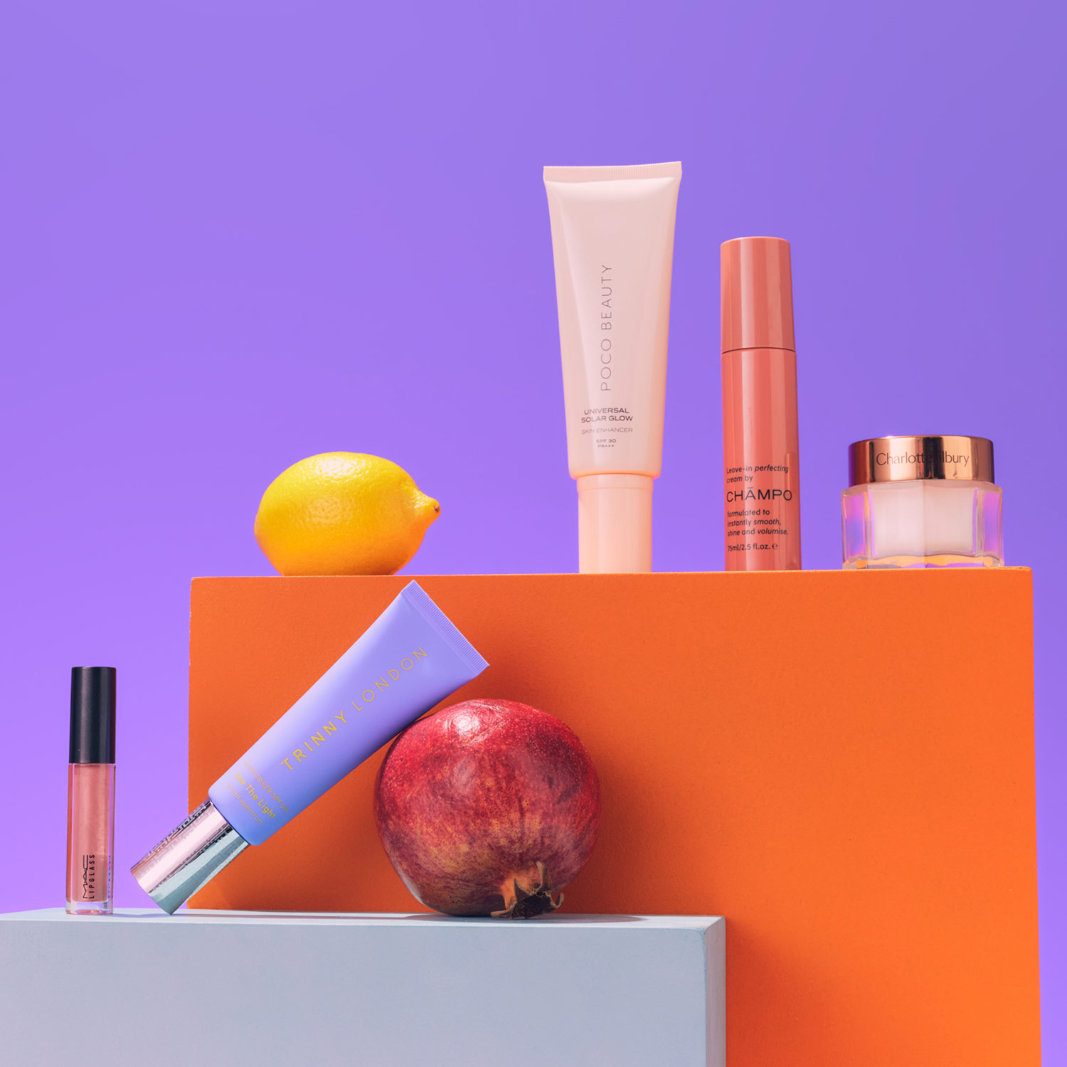 Cosmetics and fruits on colorful blocks with a purple background, featuring a lemon and pomegranate.