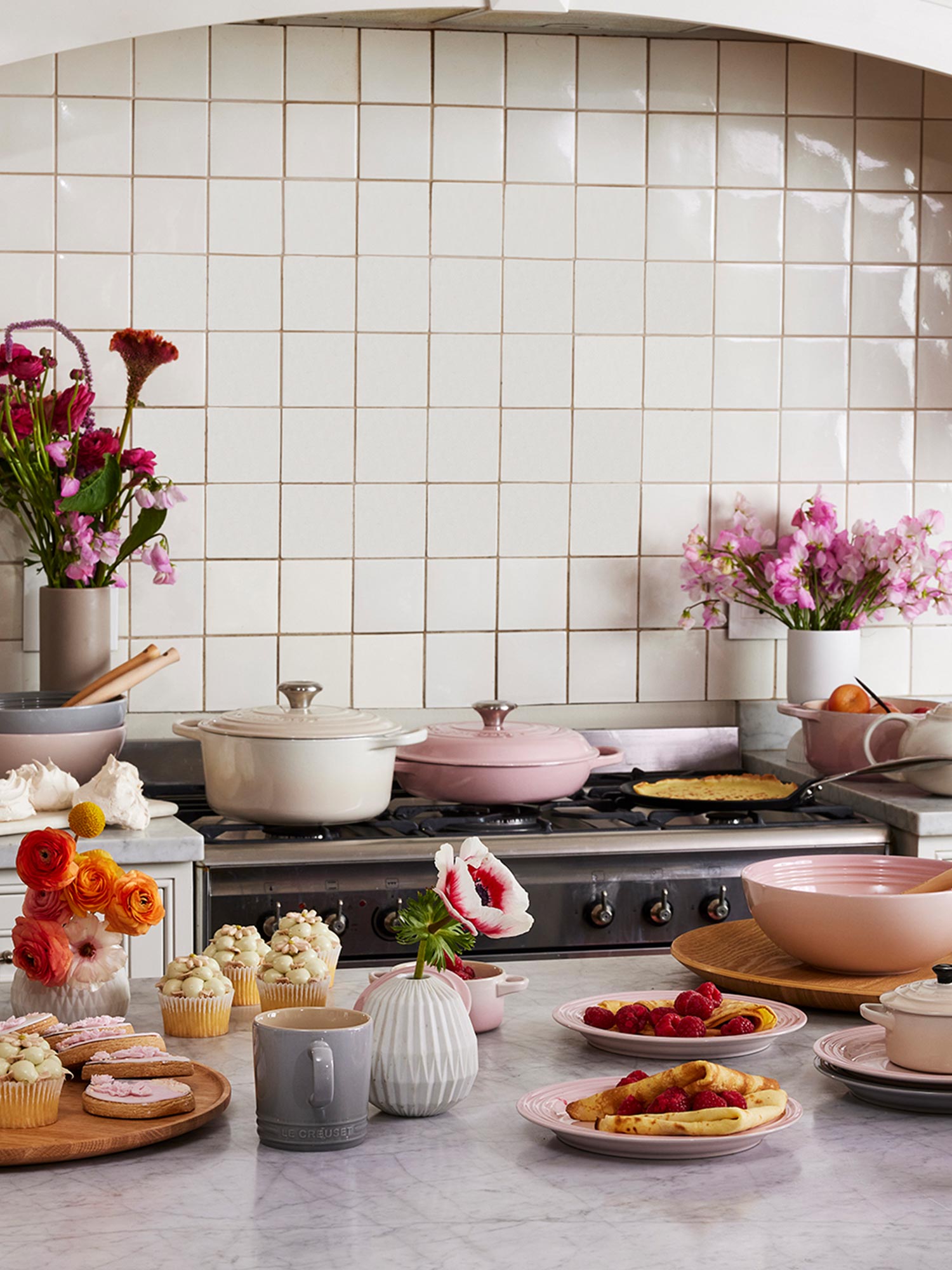 A kitchen scene with colorful flowers, cookware, and a variety of pastries on the countertop.