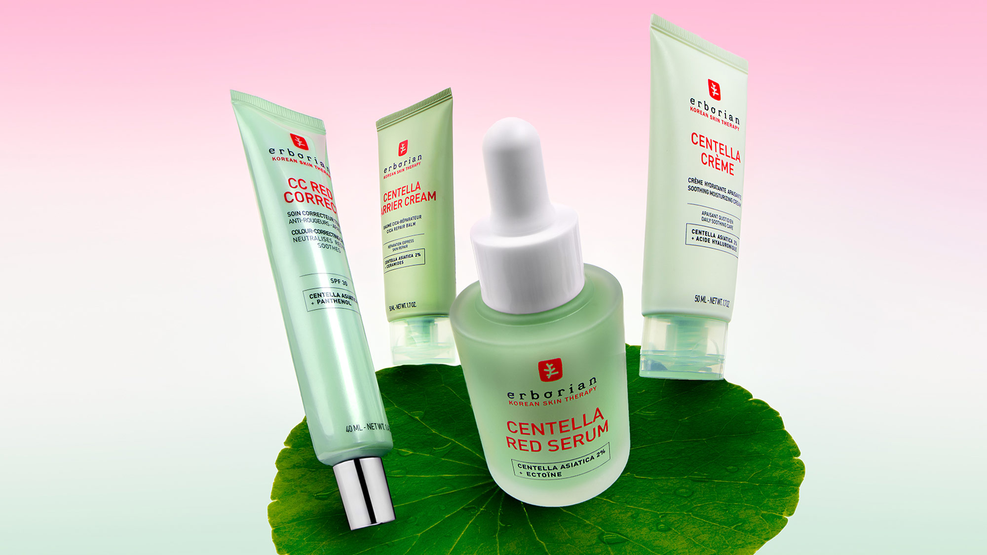 Skincare products, including a serum dropper and tubes, displayed on a large green leaf with a pink gradient background.