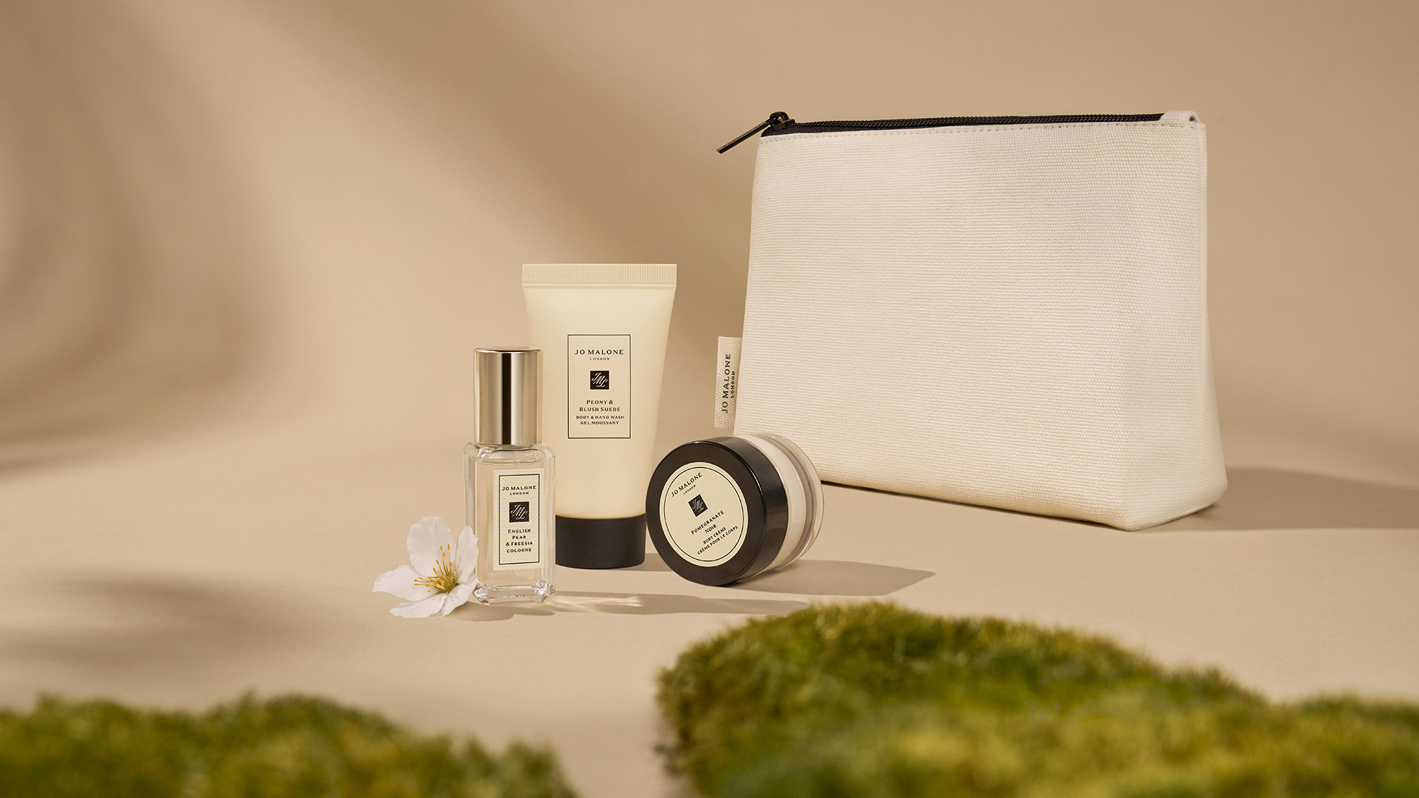 A collection of beauty products, including bottles and a pouch, displayed on a beige surface with green moss in the foreground.