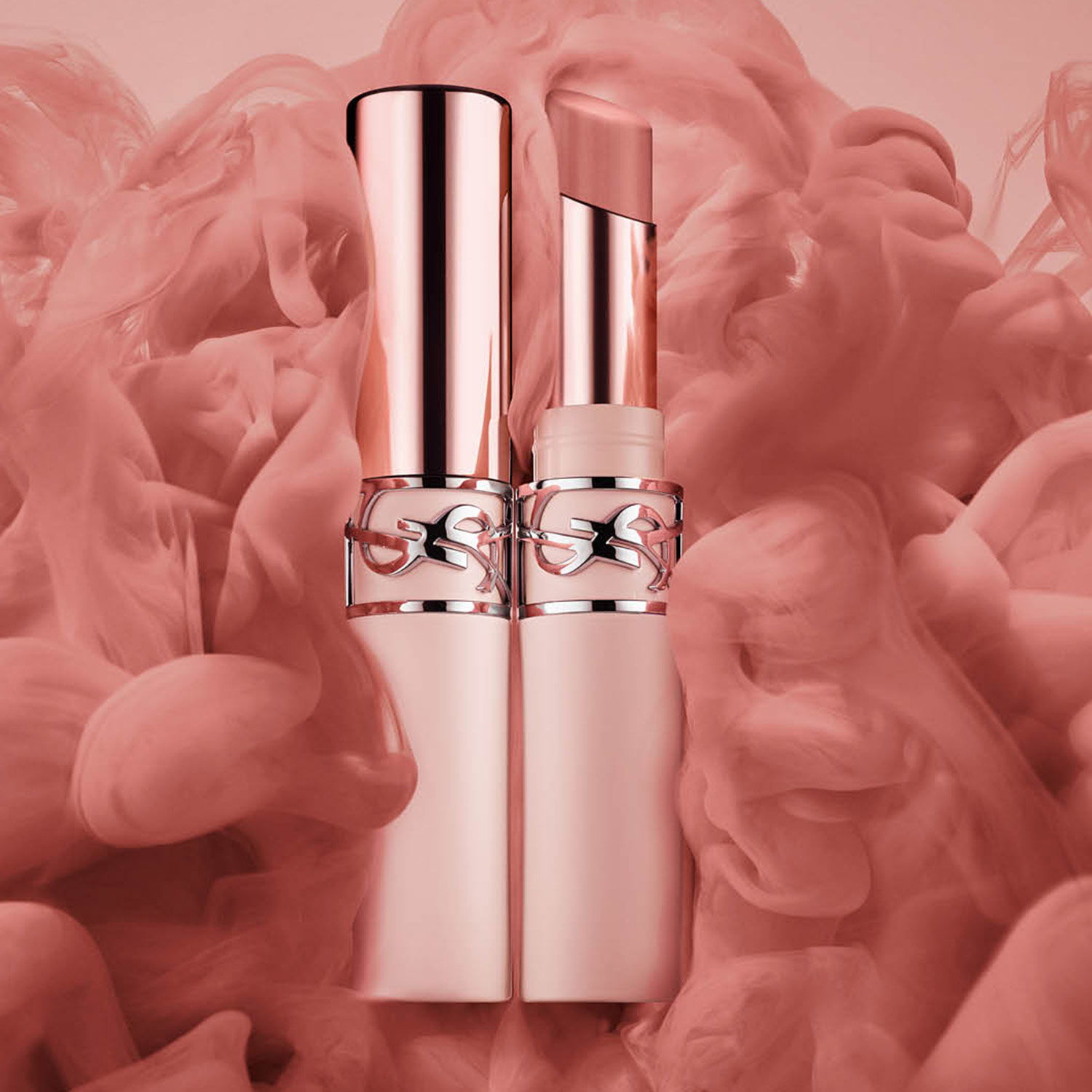 Two elegant lipstick tubes stand amidst swirling pink smoke.