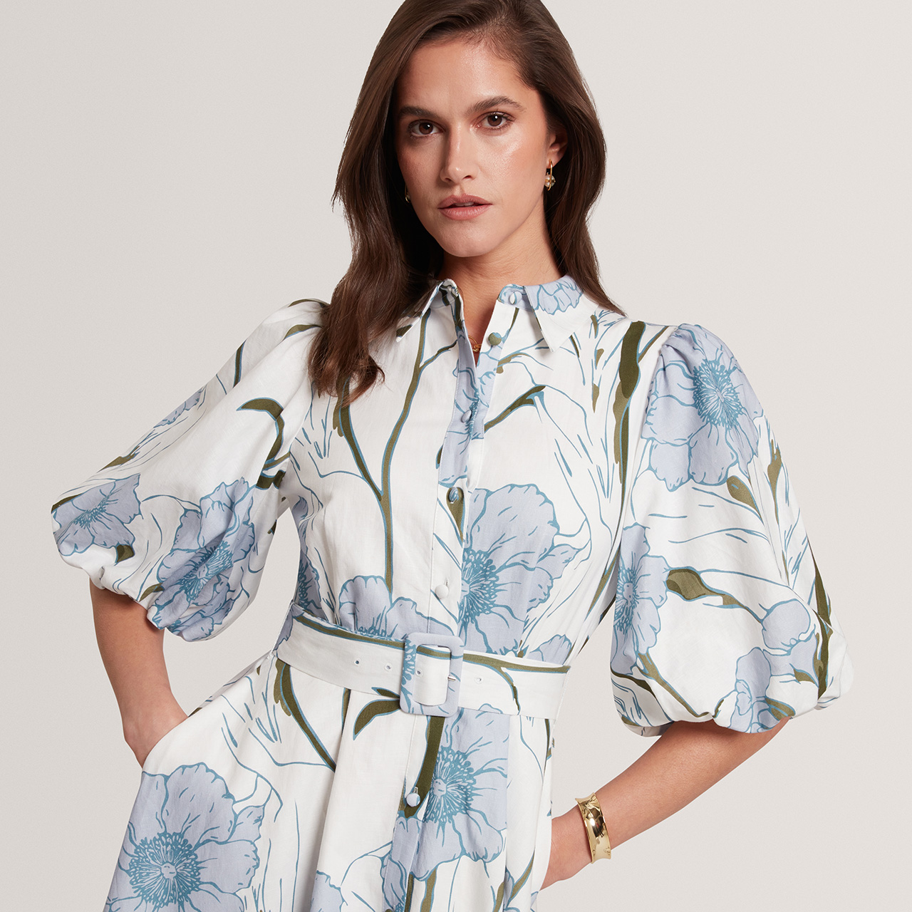 Woman wearing white shirt dress with blue floral print and puffed sleeves, cinched with matching belt