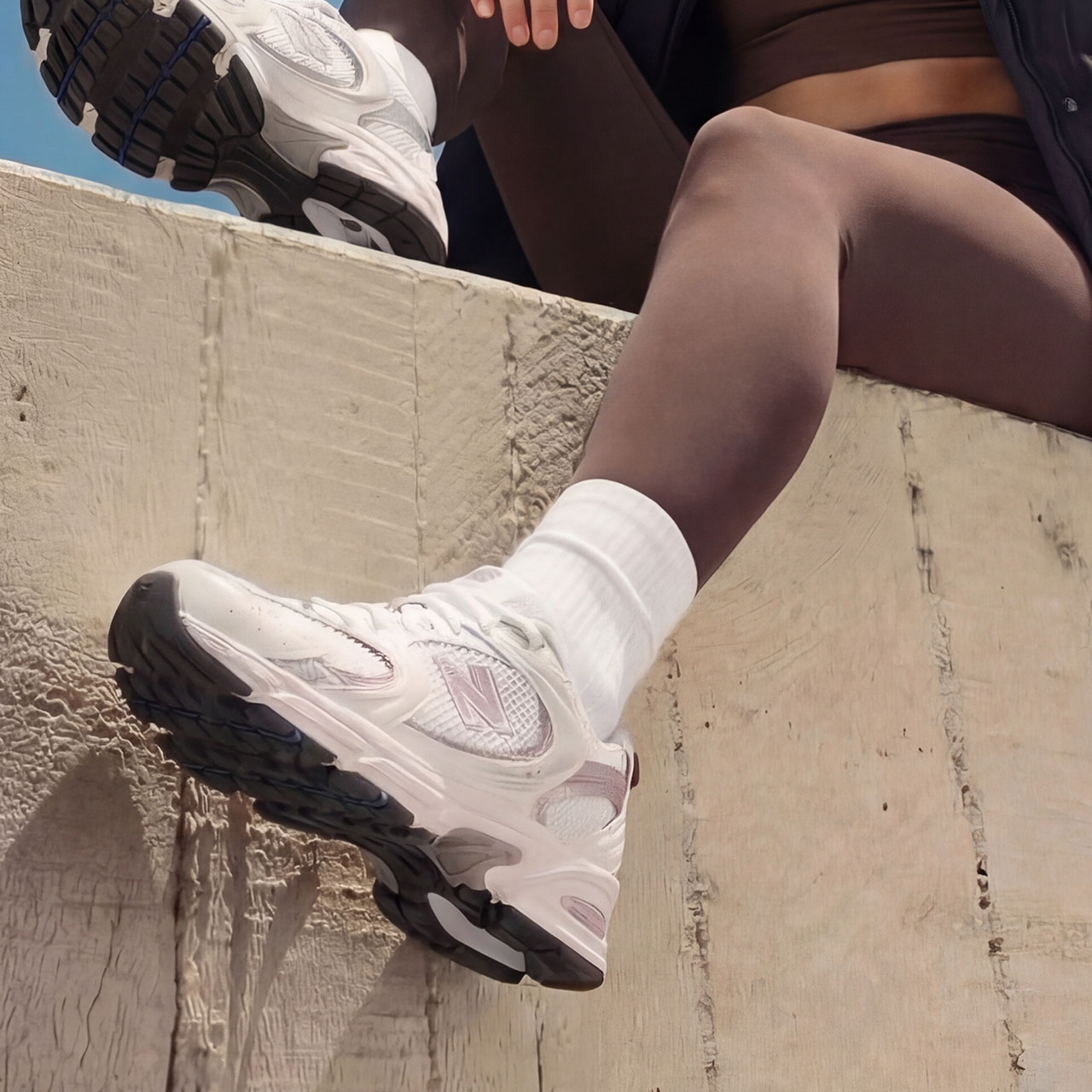 Person sitting on a ledge, wearing black leggings and white sneakers with white socks.