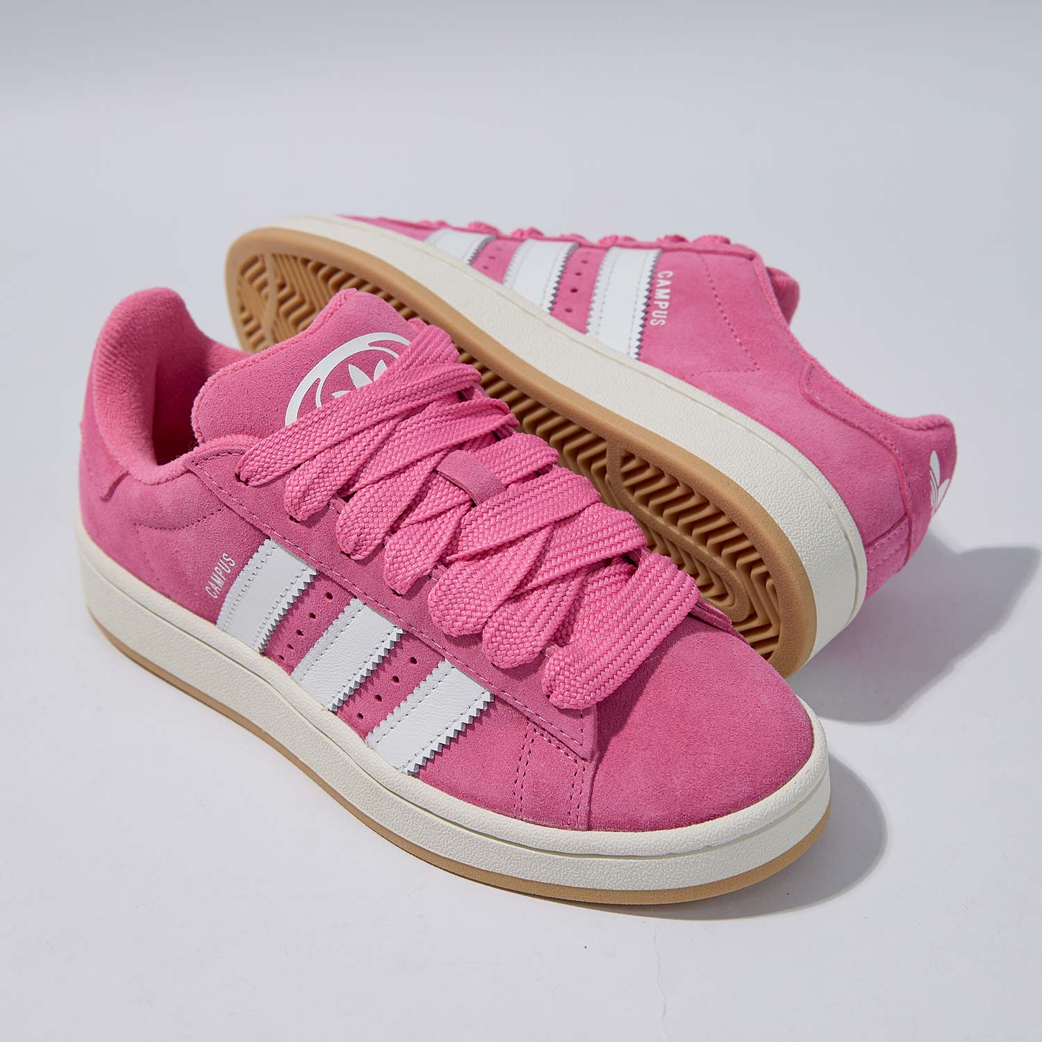 Pink sneakers with white stripes and gum soles on a plain background.