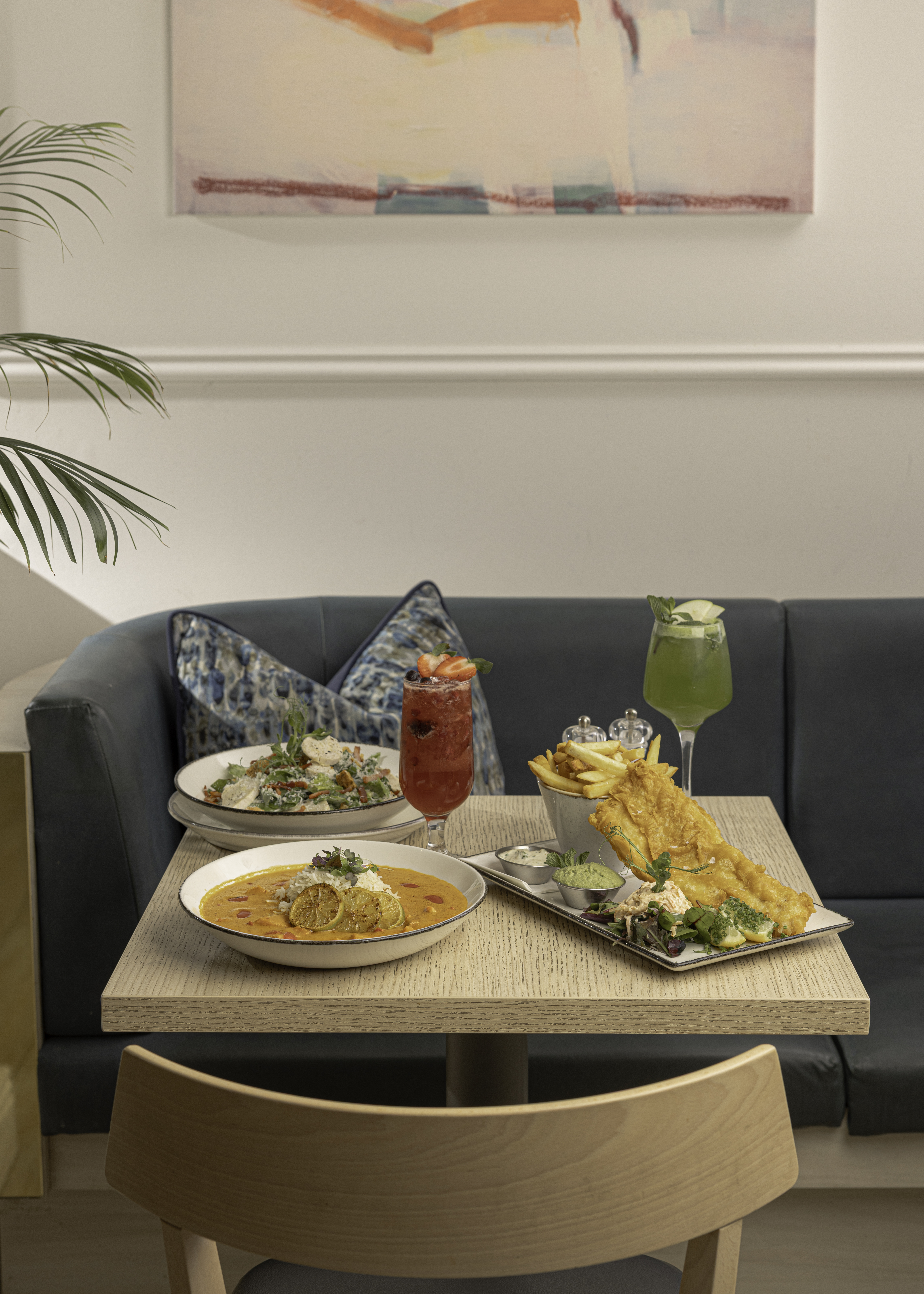 A table with seafood dishes, two colorful drinks, and a stylish, cozy dining setting.