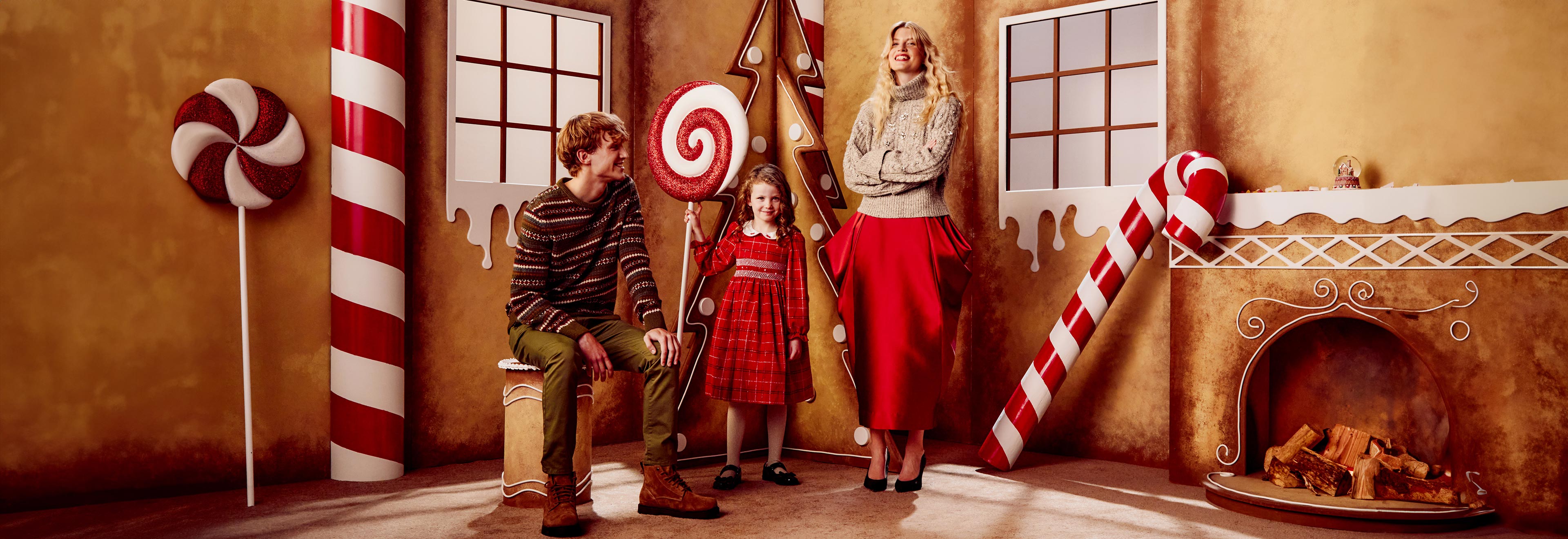 A family in a gingerbread-themed room decorated with oversized candy and a fireplace.