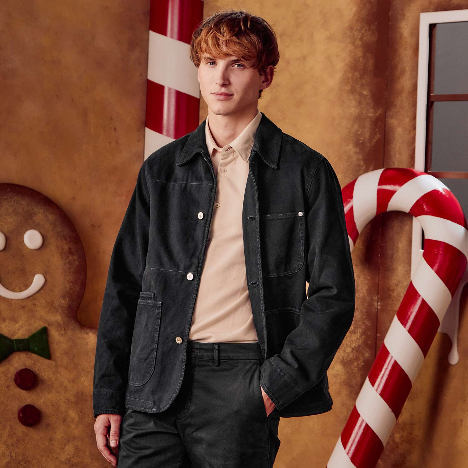 A person in a black jacket stands in a festive setting with candy canes and a gingerbread figure.