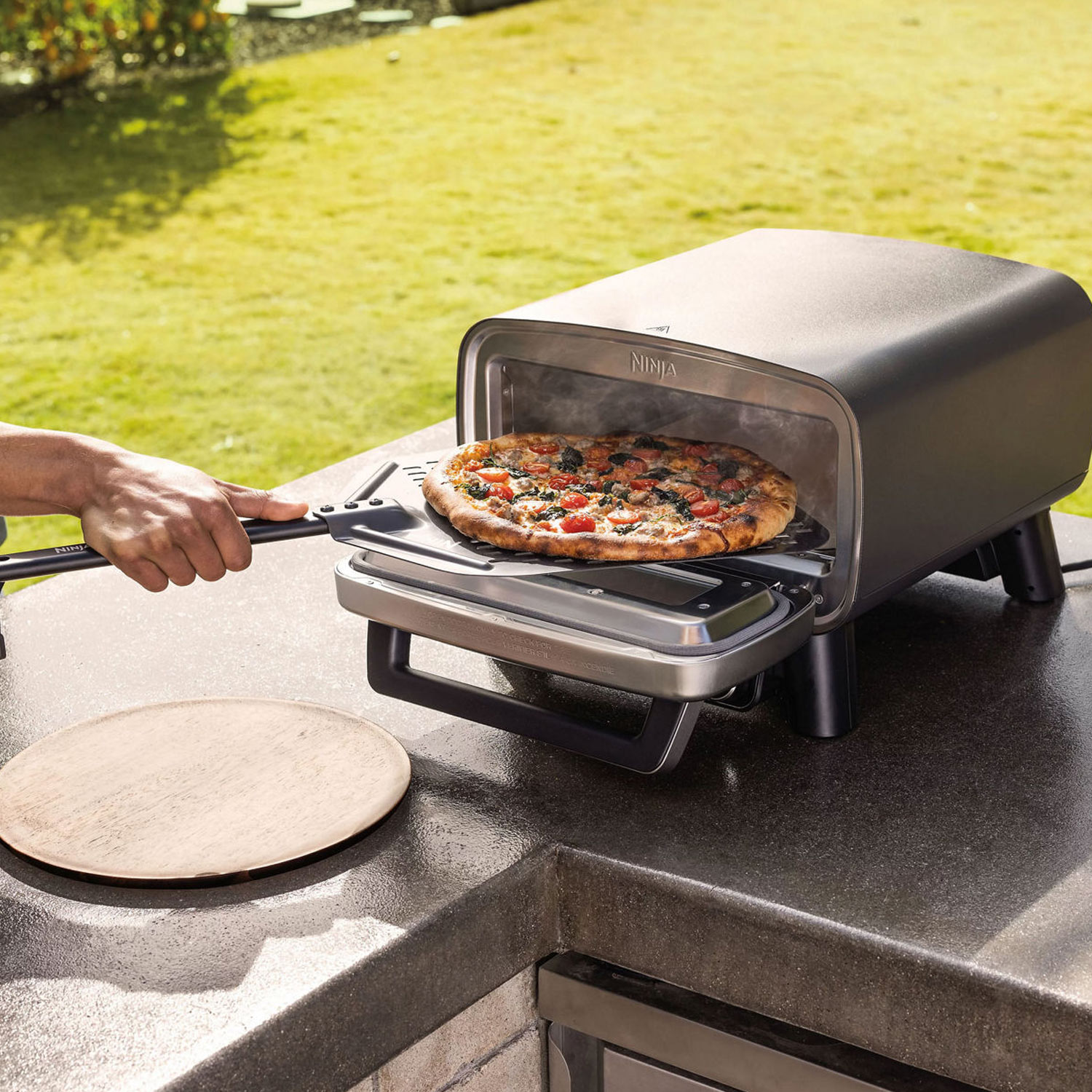 ninja pizza oven with pizza in garden