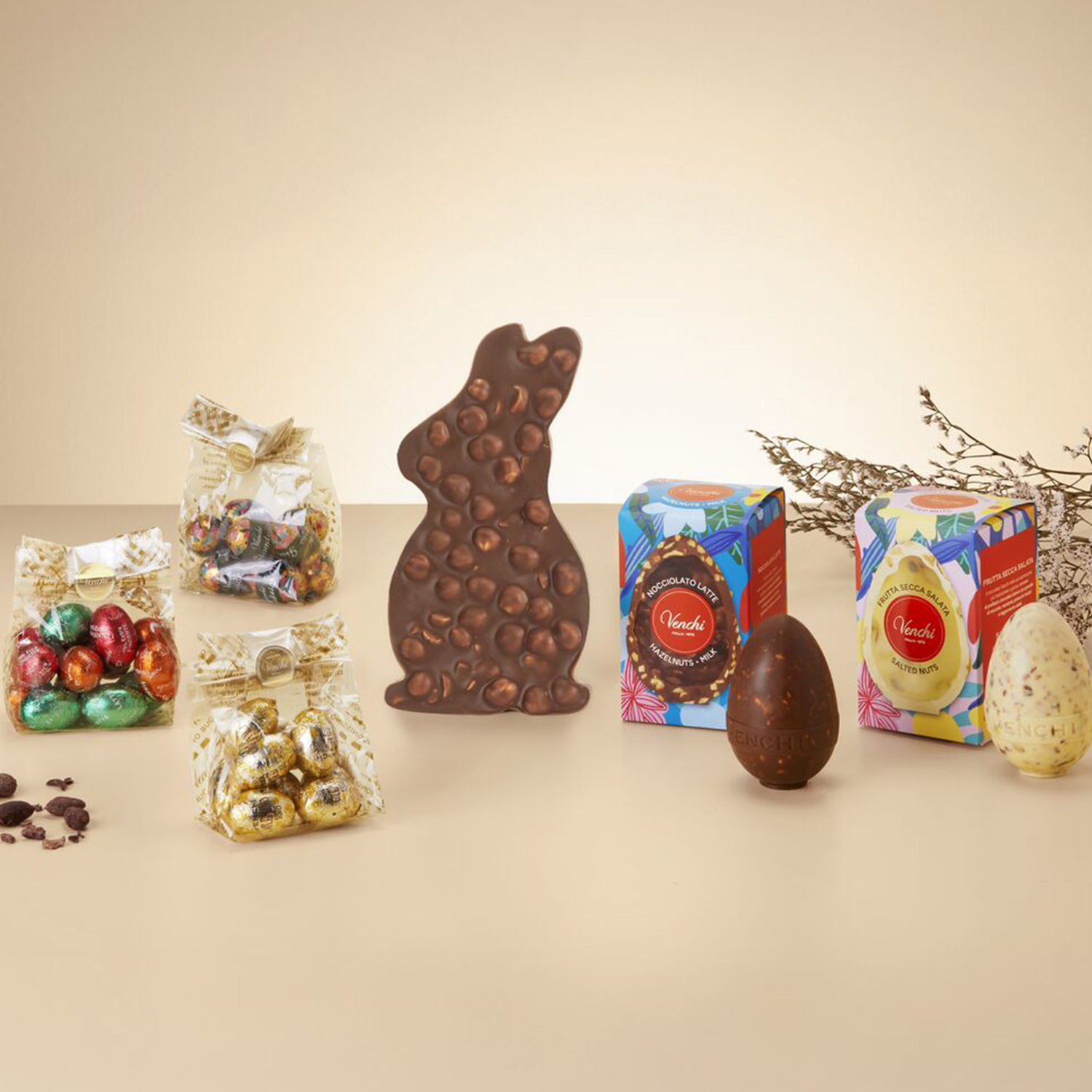 Assorted chocolate items including a chocolate bunny, colorful wrapped chocolates, and boxed chocolate eggs on a neutral background.