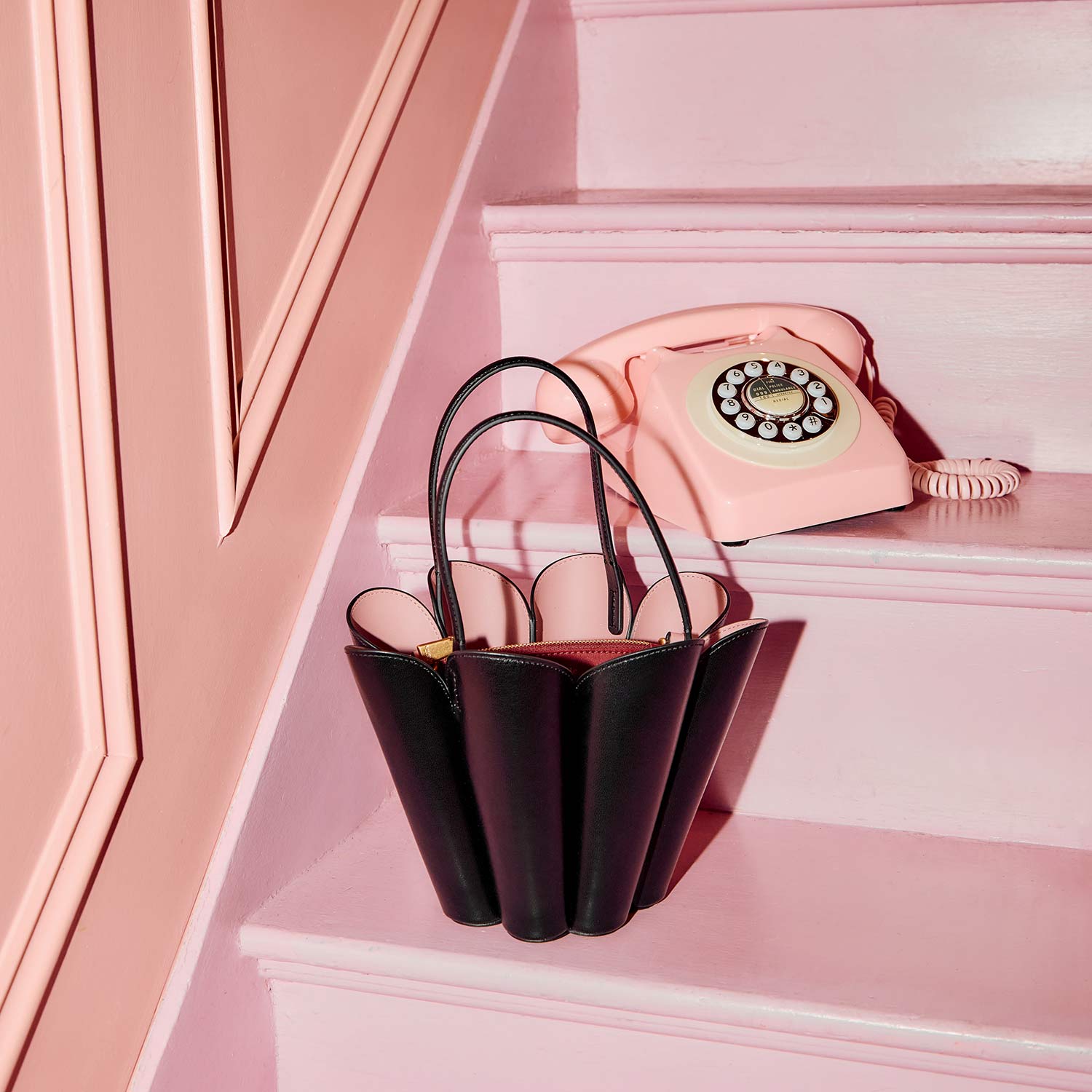 A black handbag and a pink rotary phone are placed on pink stairs.
