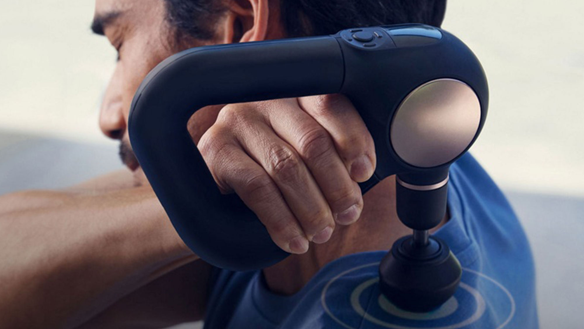 Man holding blue Therabody massage device against shoulder outdoors, demonstrating muscle relaxation technology