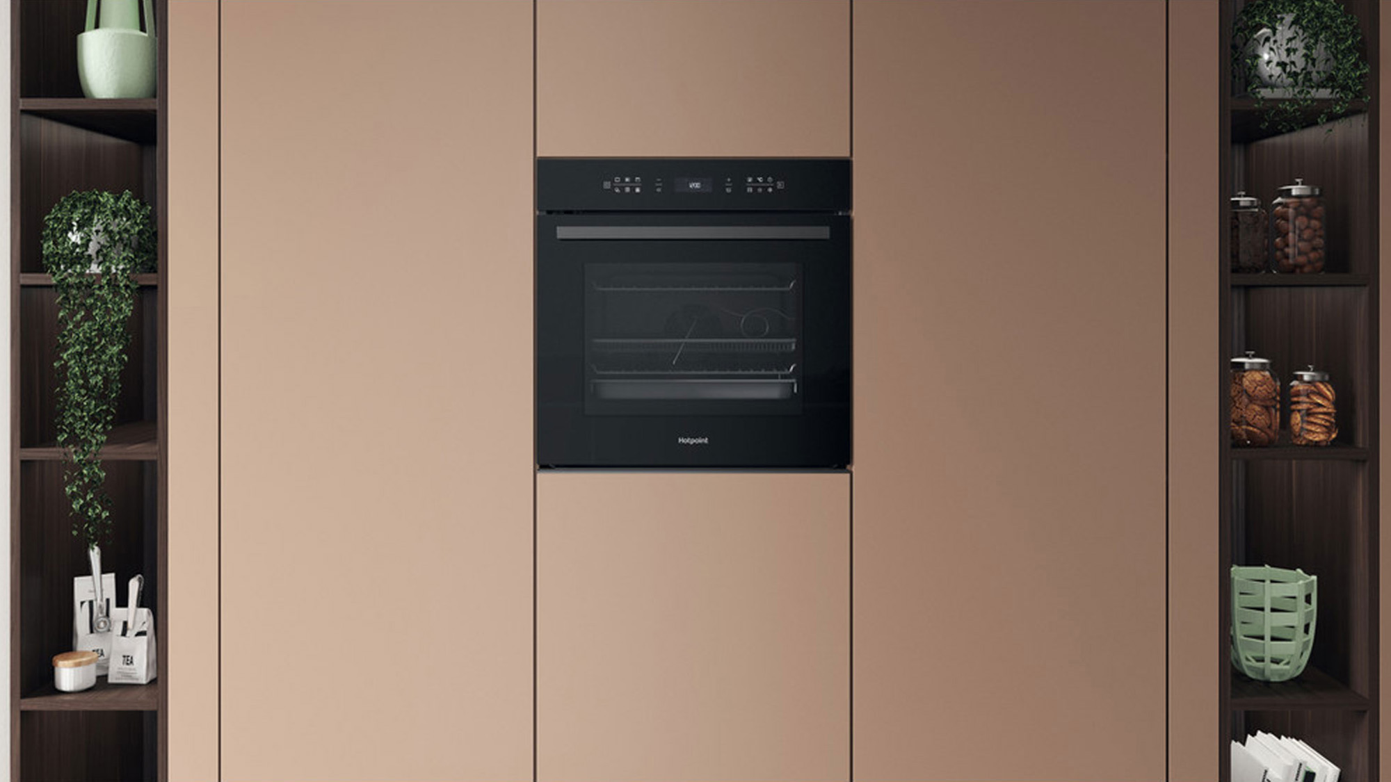 Built-in black oven set in a tan kitchen wall with shelves holding plants, jars, and kitchen items on either side.