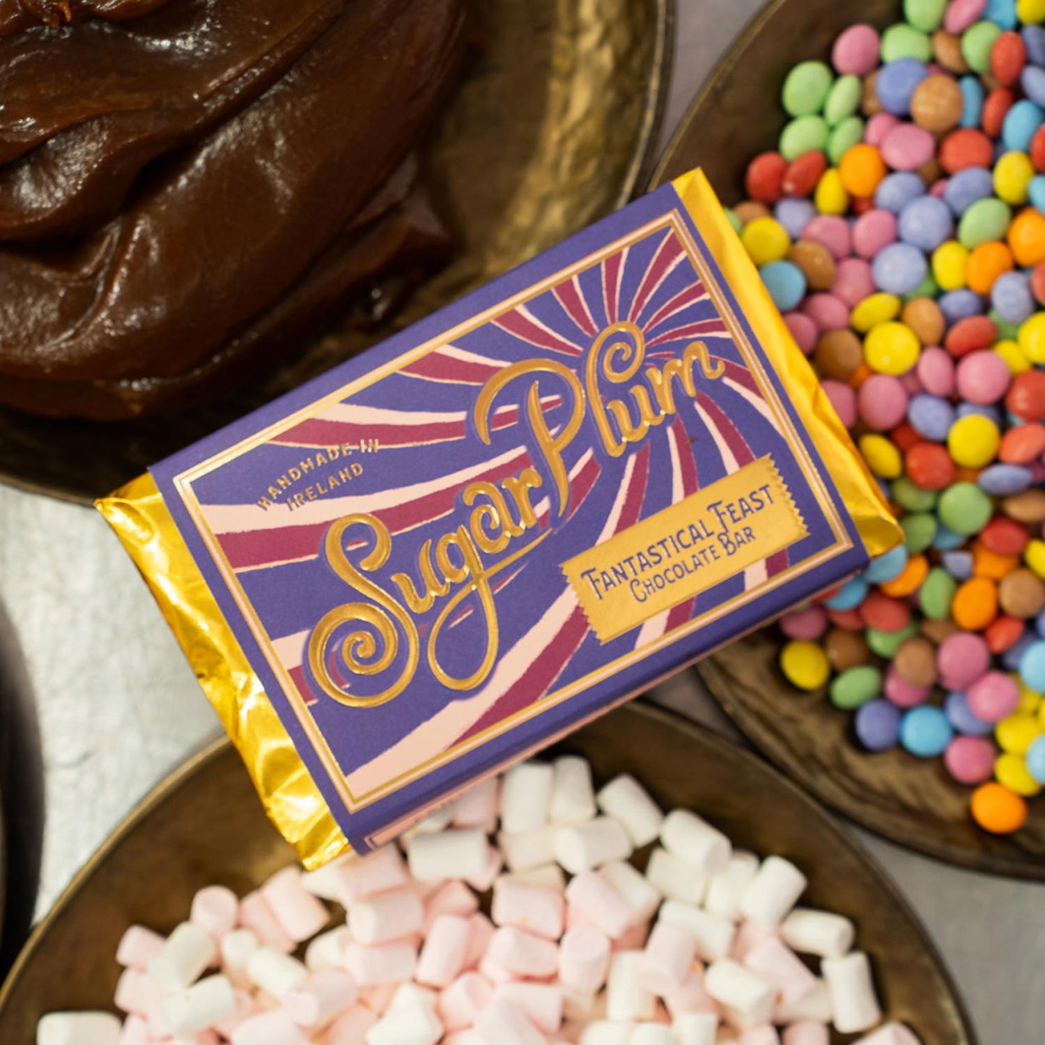 Sully Fantastical Feast chocolate bar with purple packaging featuring ornate gold lettering, displayed alongside colourful sweets