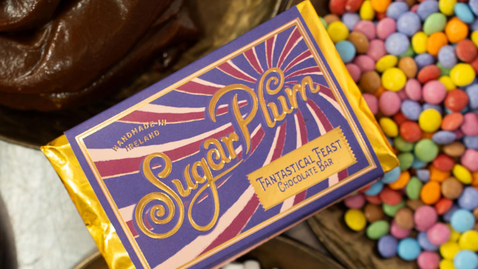 Sully Fantastical Feast chocolate bar with purple packaging featuring ornate gold lettering, displayed alongside colourful sweets