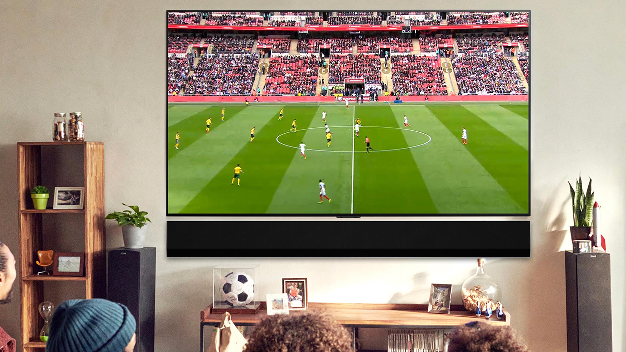 Large flat-screen TV mounted on wall displaying live football match with stadium crowd, in modern living room setting